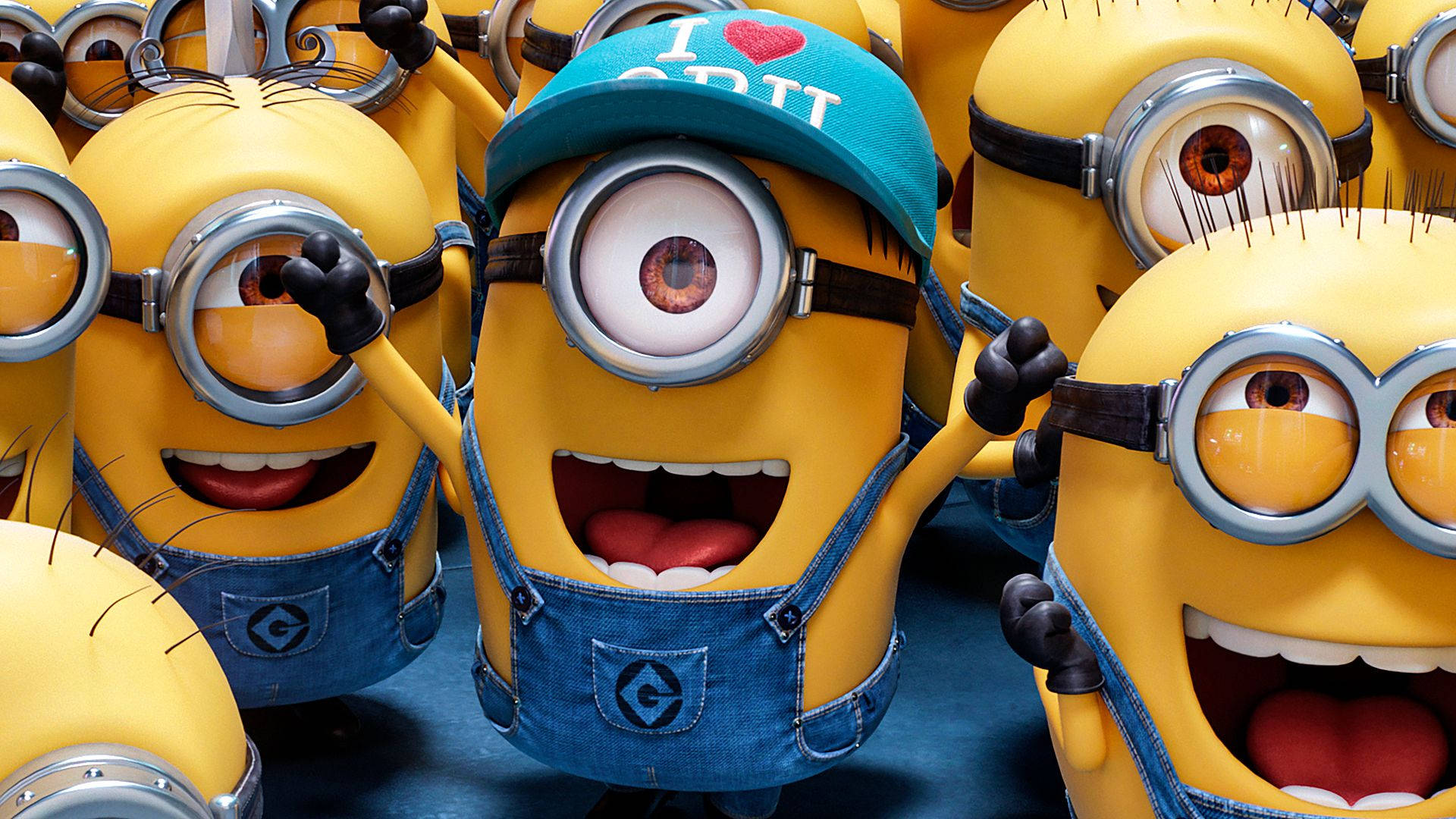 快樂的Minions身穿藍色吊帶褲和護目鏡，與一個戴帽子的擺姿勢。 — 神偷奶爸 GIF 壁紙