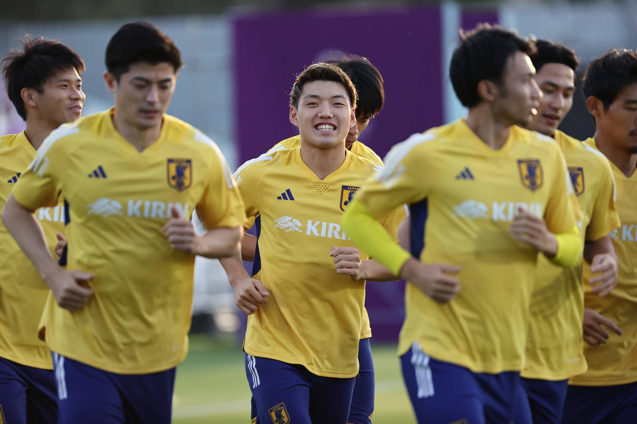 Football Players 桌布 壁紙 — 一群身穿黃色球衣的日本足球運動員在草地上慢跑，神情專注。