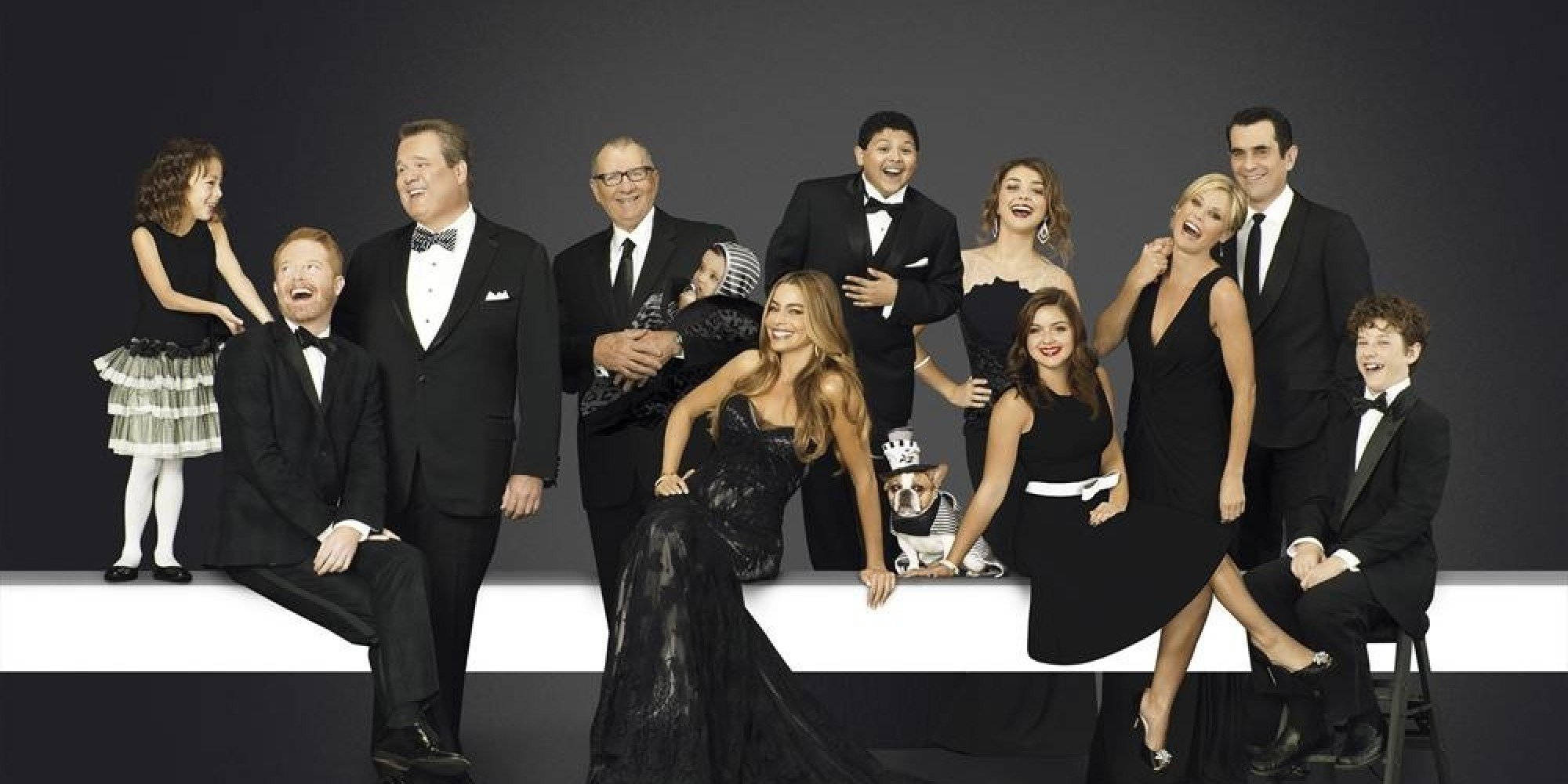 Modern Family 桌布 壁紙 — 一群身穿黑色正裝的演員在黑暗背景下，於簡約白色平台上愉快地擺姿勢。