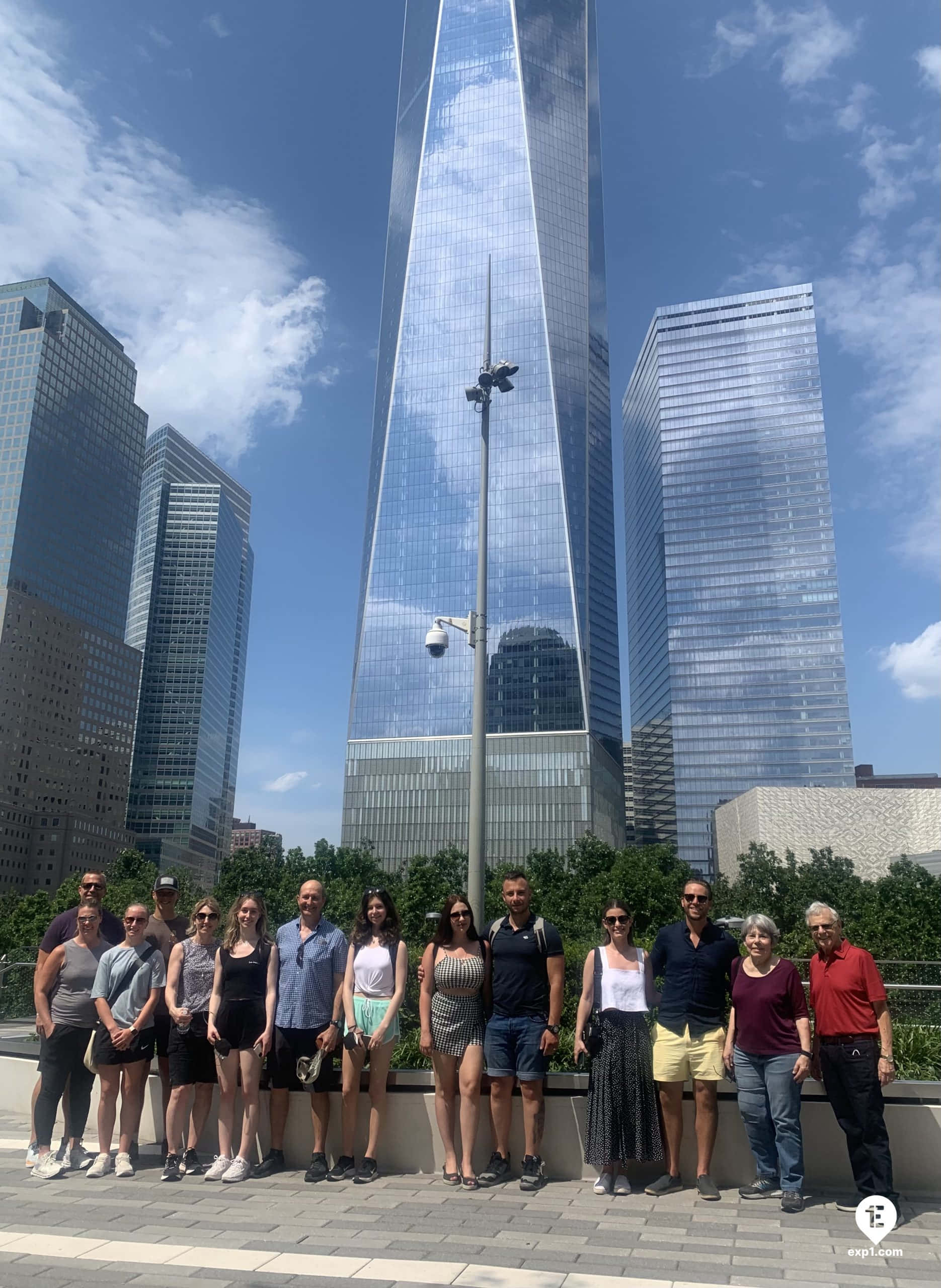 Blue Sky 桌布 壁紙 — 一群遊客在反射的One World Trade Center前，在明亮的藍天和散落的雲朵下拍照留念。