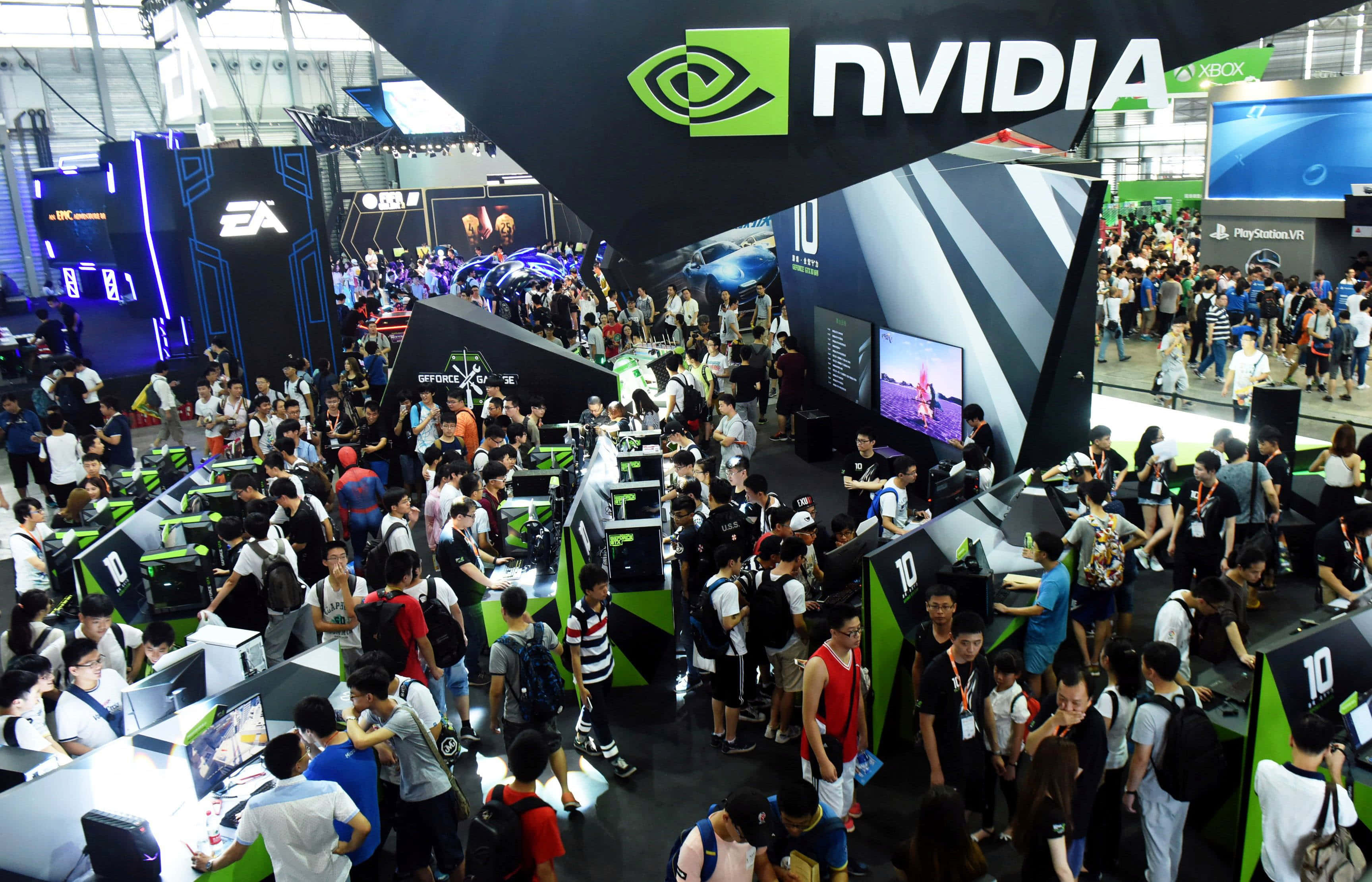 nvidia 桌布 壁紙 — 一群遊戲玩家聚集在熙熙攘攘的科技展會上的NVIDIA遊戲展位周圍，展位配有發光的螢幕和品牌展示。