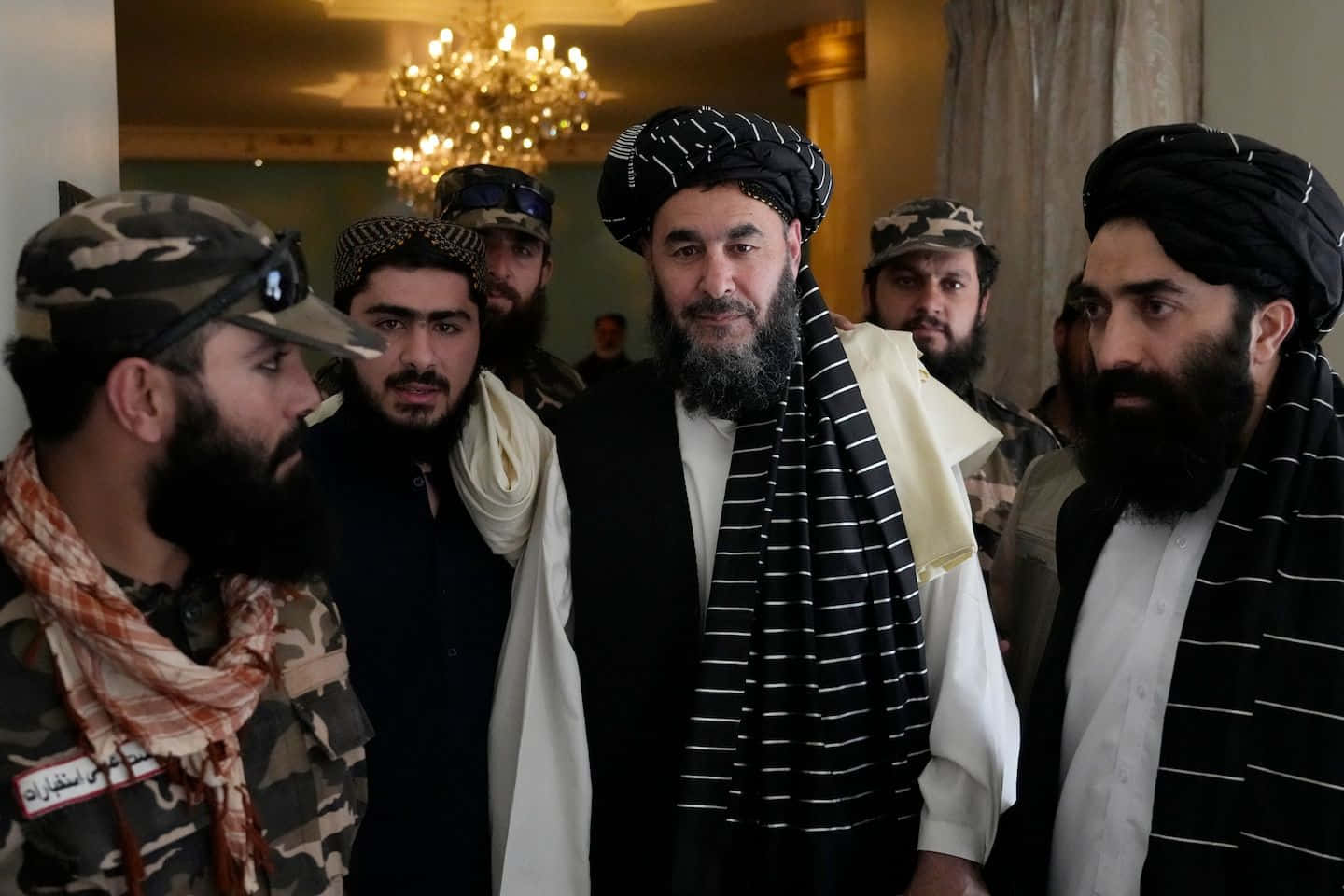 Taliban 桌布 壁紙 — 一群阿富汗男子身穿傳統頭巾和軍事裝備，在室內吊燈下站在一起。