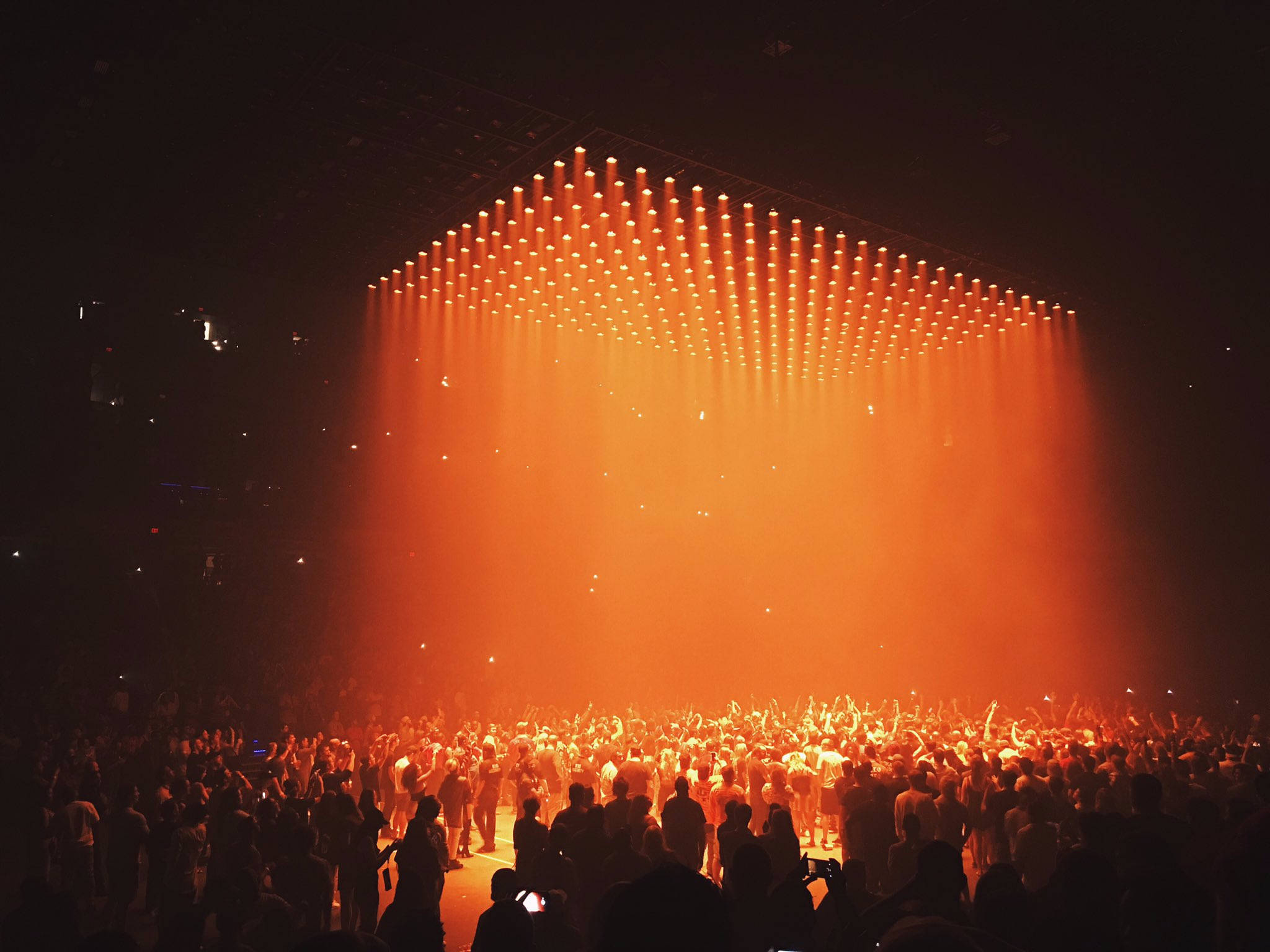 kanye west saint pablo 桌布 壁紙 — 一群音樂會觀眾在舞台上方懸掛的巨大橙色發光燈光網格襯托下形成剪影。