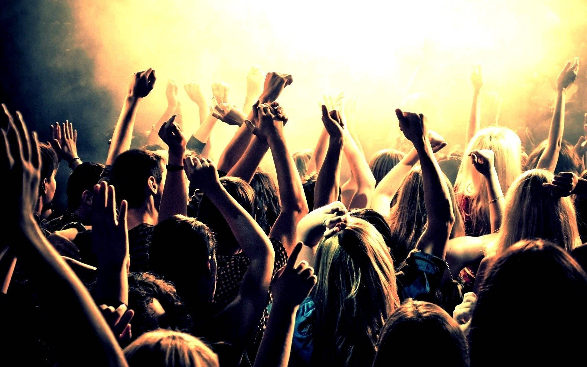 Party 桌布 壁紙 — 一群音樂會觀眾在金色舞台燈光和煙霧中舉起手臂。