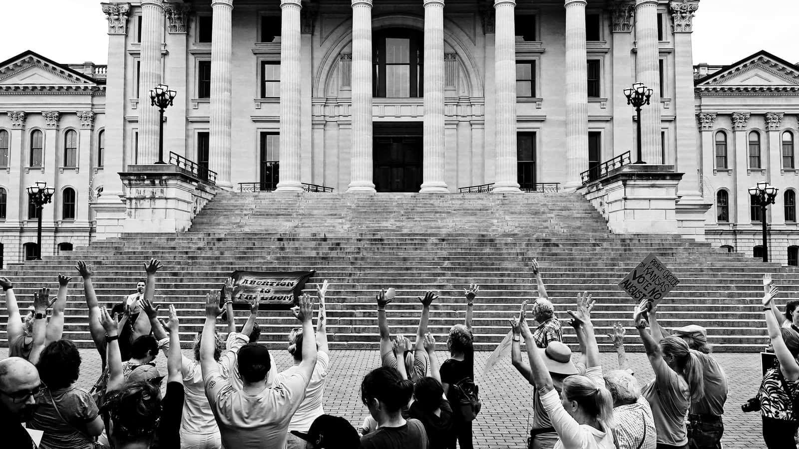 Politics 桌布 壁紙 — 一群黑白人群在宏偉的新古典主義建築前舉起拳頭和標語，建築有高大的柱子和寬闊的石階。