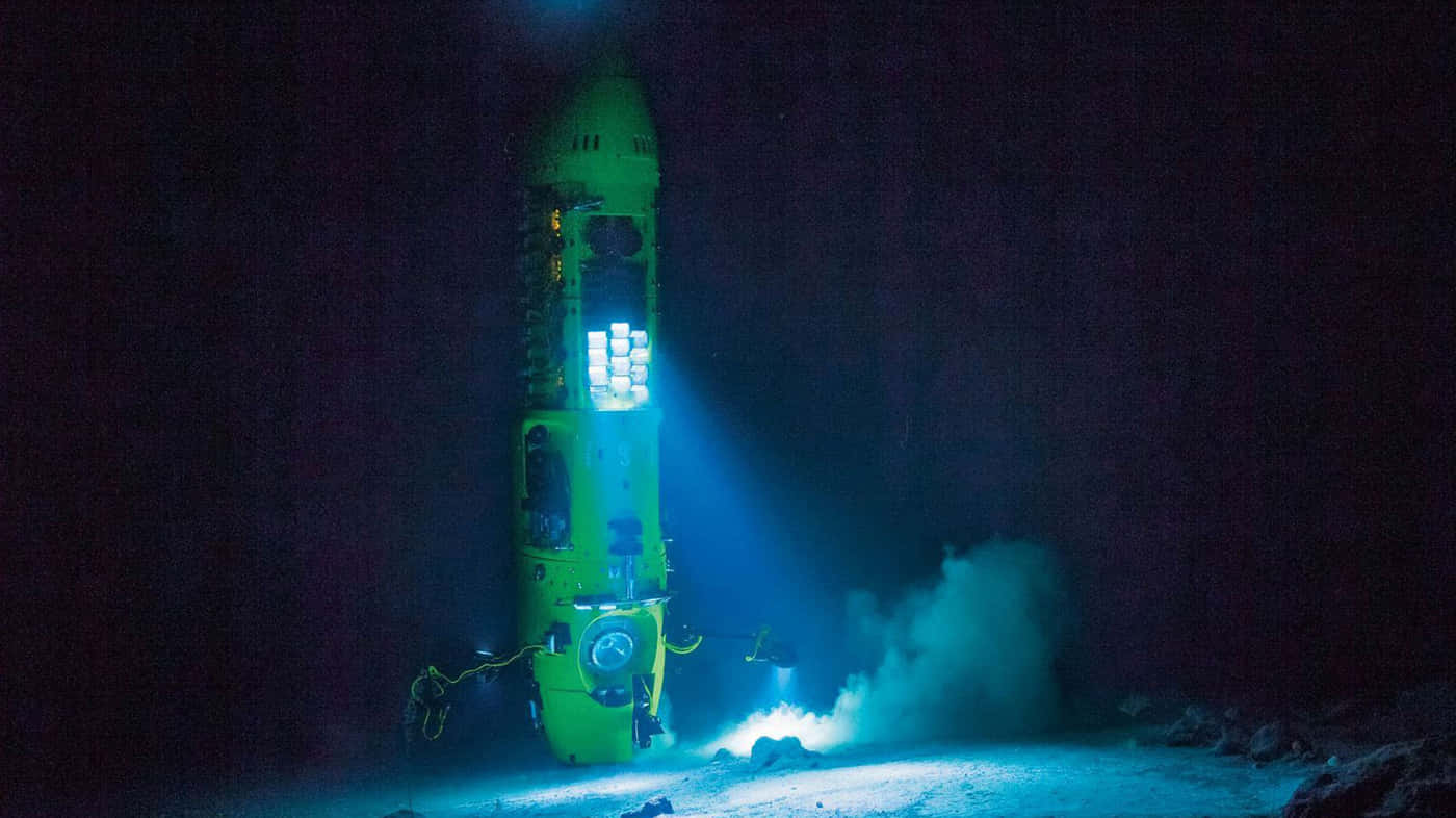 Mariana Trench 桌布 壁紙 — 一艘亮綠色的潛水器在自身燈光下發光，下降至黑暗的海底溝渠，揚起沉積物。