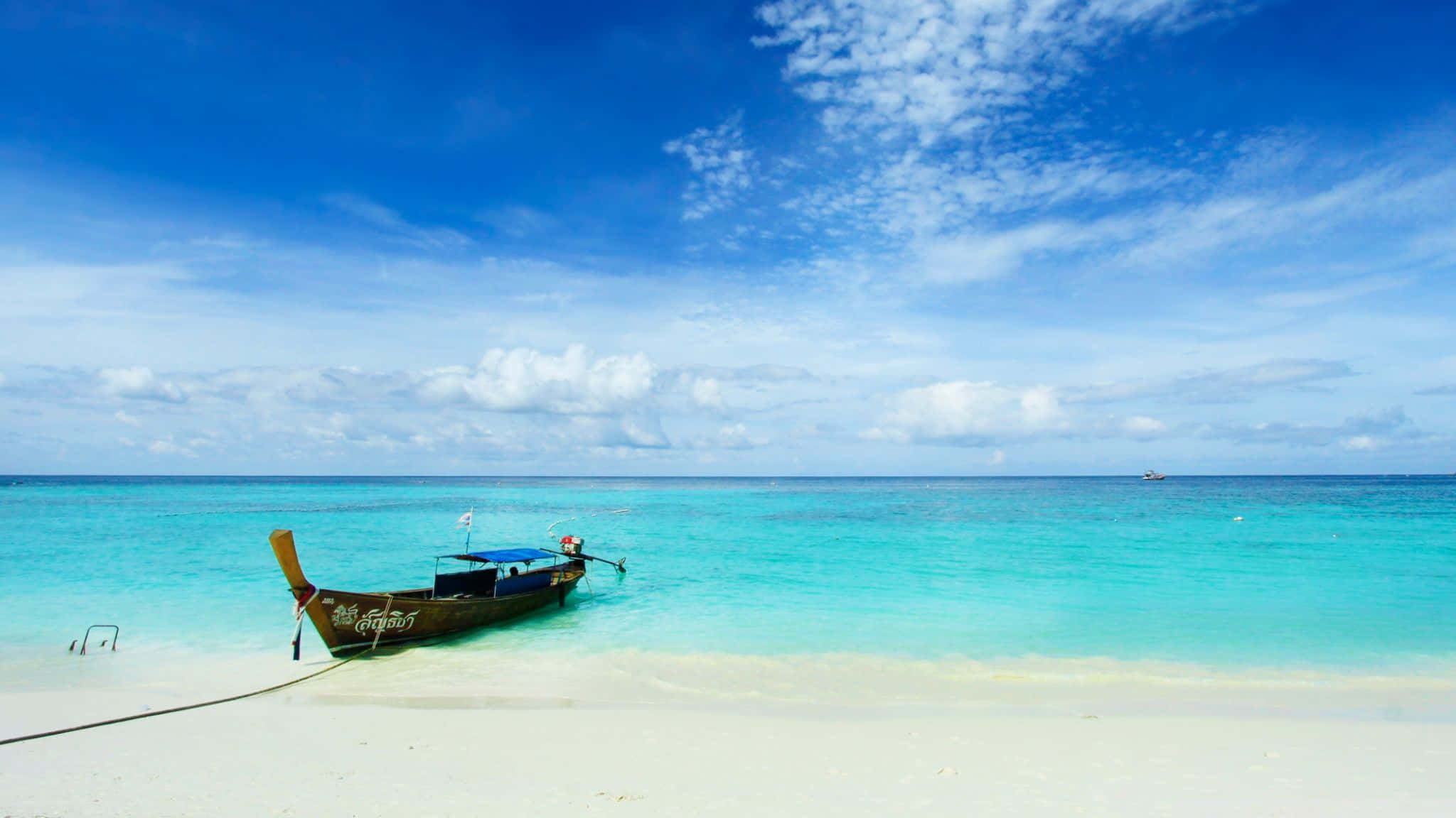 Bali Beach 桌布 壁紙 — 一艘傳統木製長尾船停泊在純淨的白色沙灘上，旁邊是碧綠的海水，上方是晴朗的藍天，點綴著幾朵白雲。