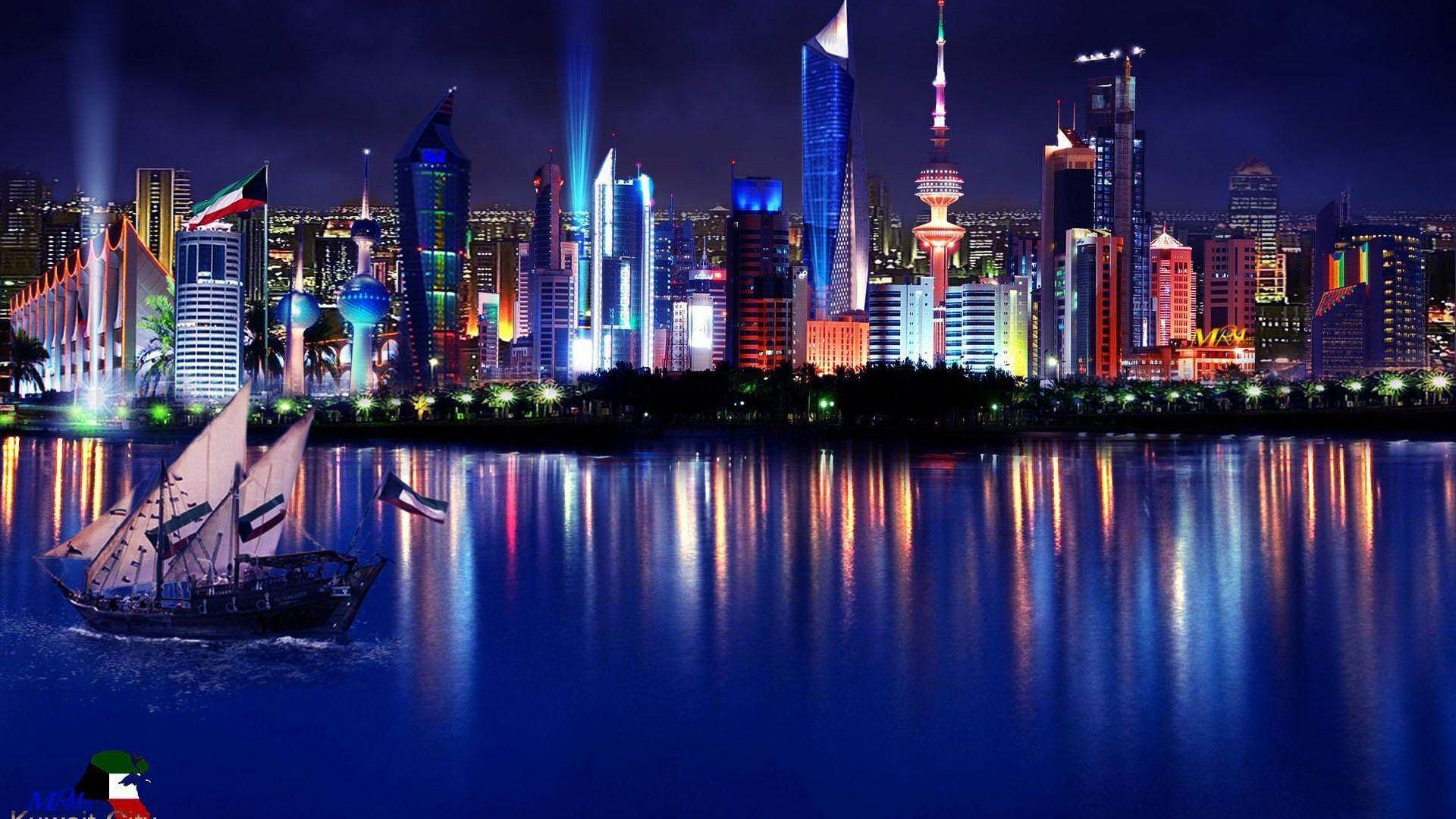 科威特 桌布 壁紙 — 一艘傳統的獨桅帆船在夜晚航行經過燈火輝煌的科威特城市天際線，水面倒映出鮮豔的光影。