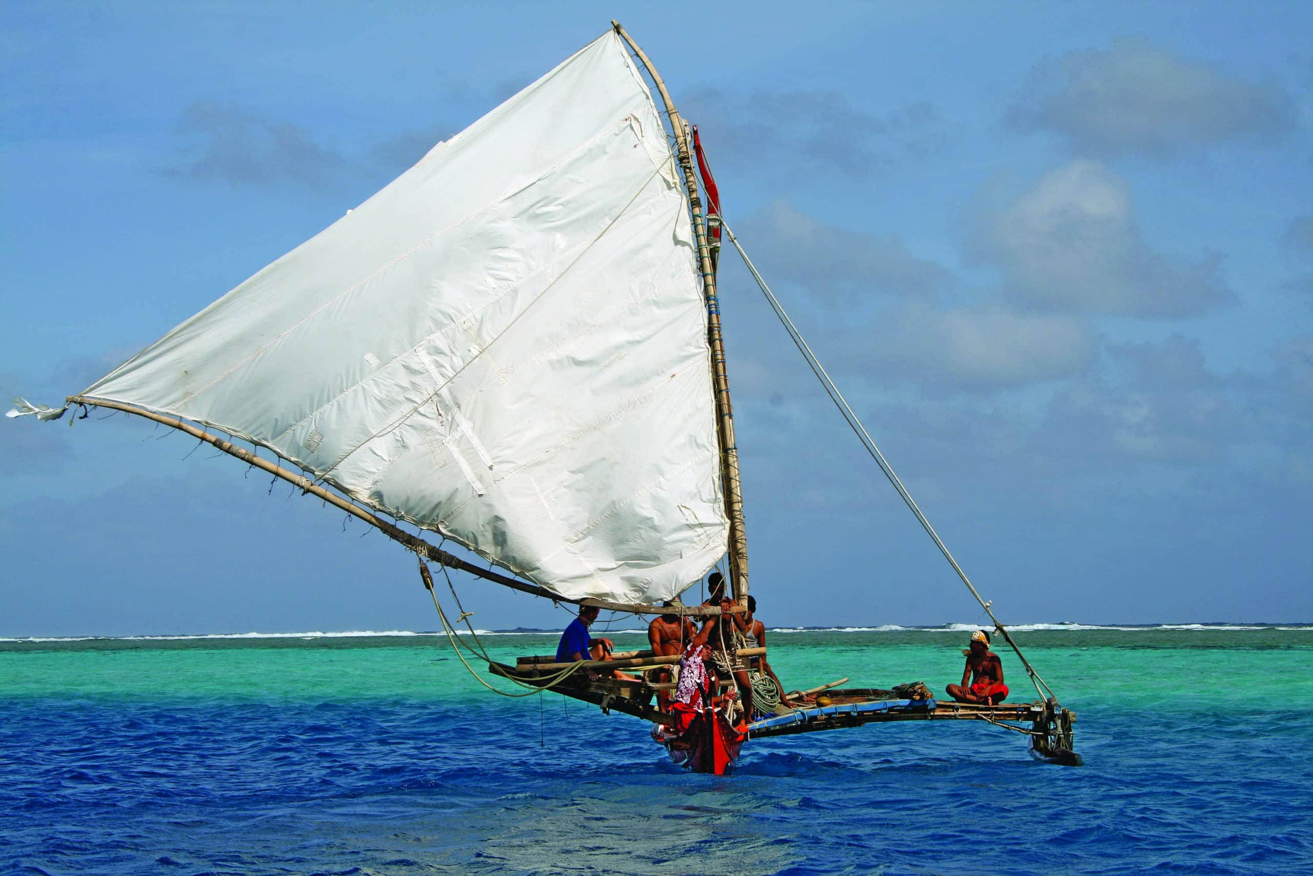 Micronesia 桌布 壁紙 — 一艘傳統的舷外支架帆船，帶著巨大的白色帆，在部分多雲的藍天下，滑過充滿活力的碧綠海水。