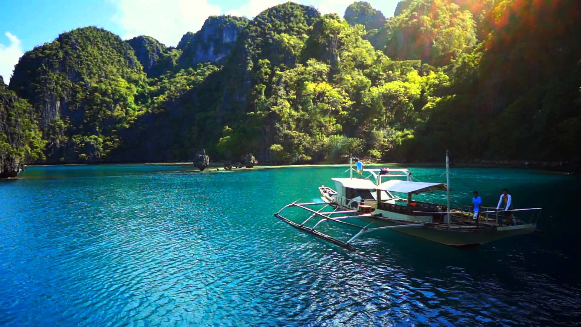 Philippines 桌布 壁紙 — 一艘傳統的菲律賓舷外支架船在明媚陽光下，滑過被翠綠喀斯特島嶼環繞的碧綠海水。