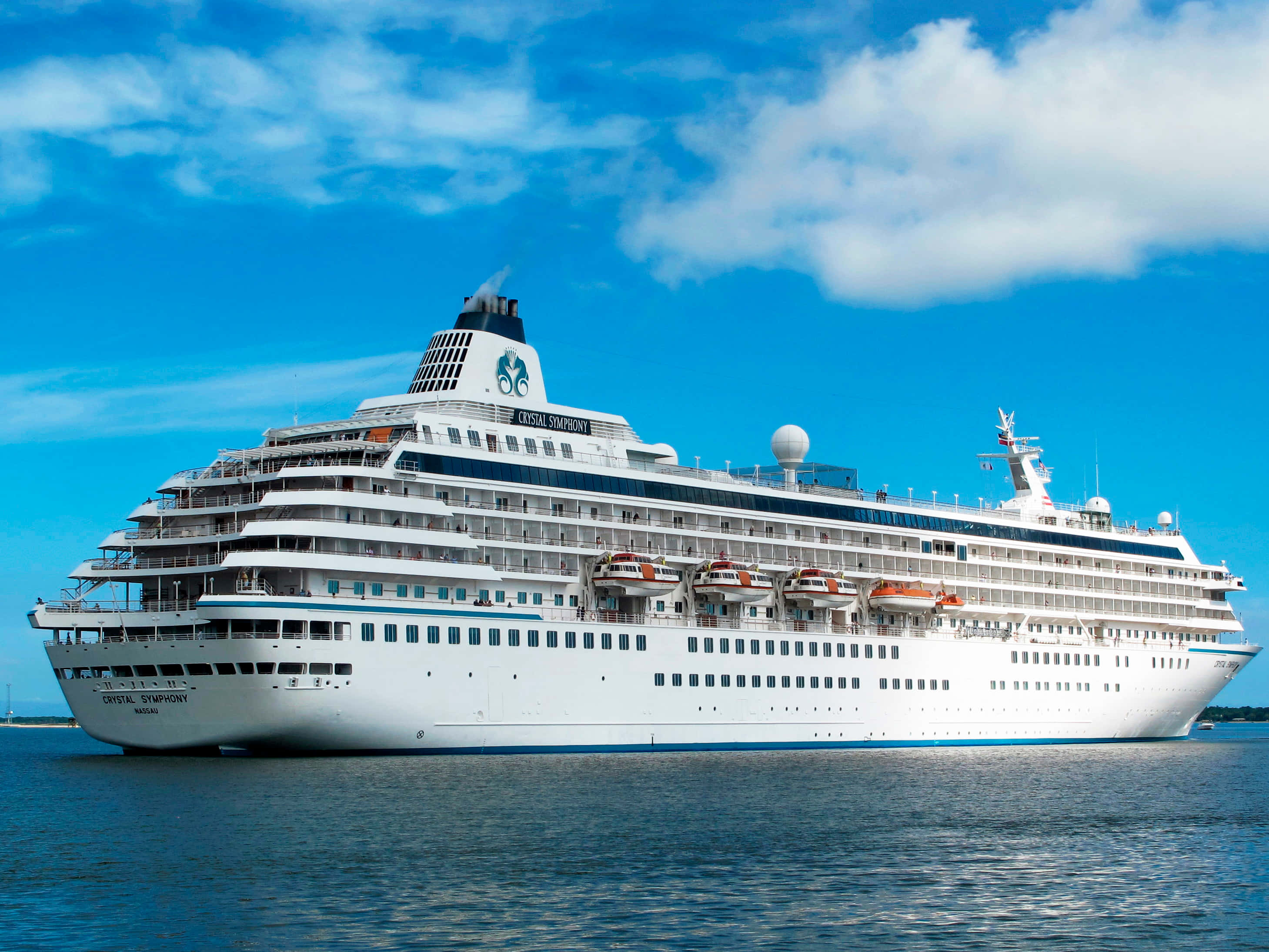 郵輪 桌布 壁紙 — 一艘名為 Crystal Symphony 的巨型白色郵輪在深藍色海面上平靜航行，天空湛藍，白雲朵朵。