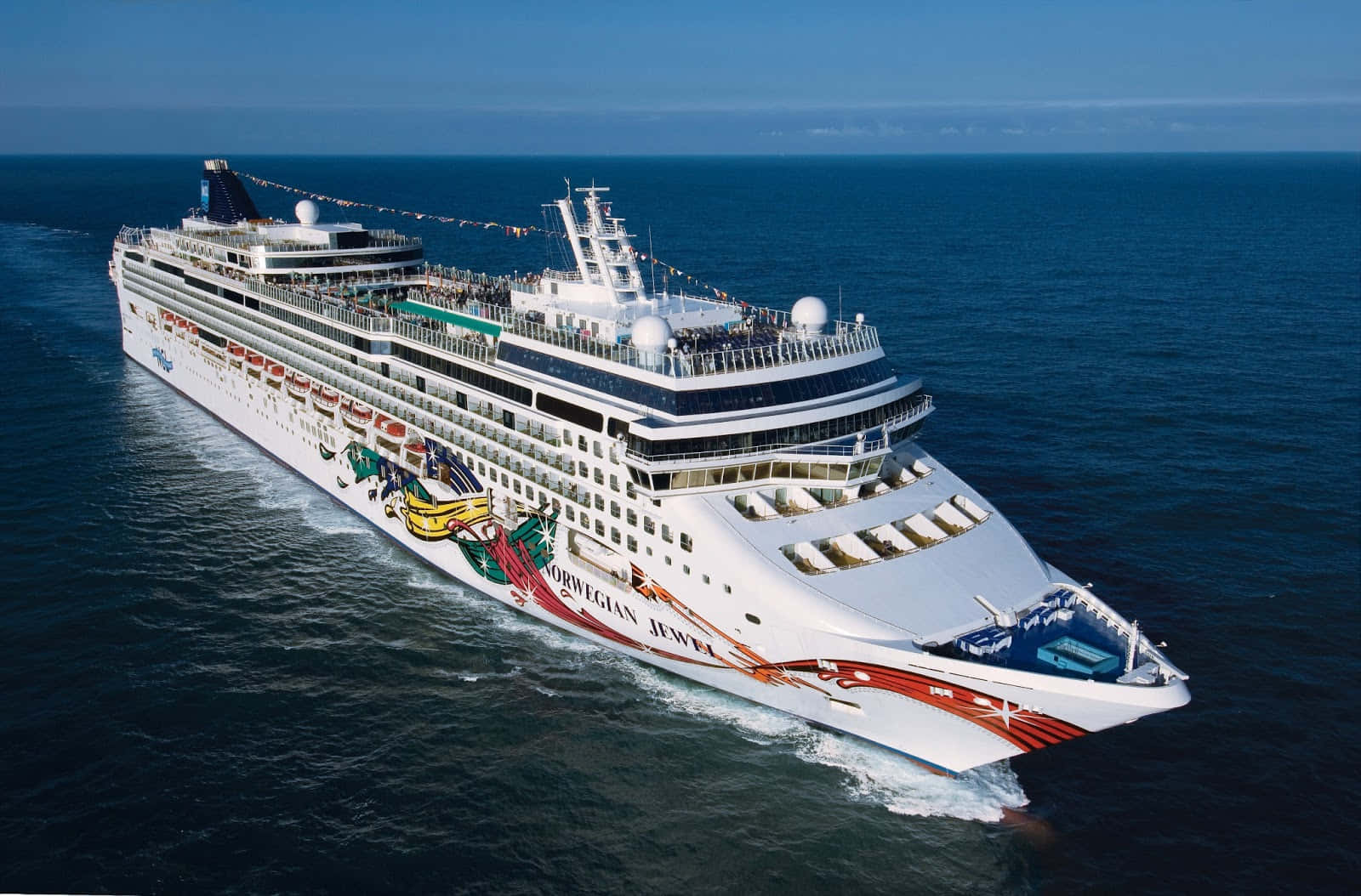 船 桌布 壁紙 — 一艘名為 Norwegian Jewel 的巨型白色郵輪在晴朗天空下航行於深藍色海洋，留下泡沫般的尾跡。