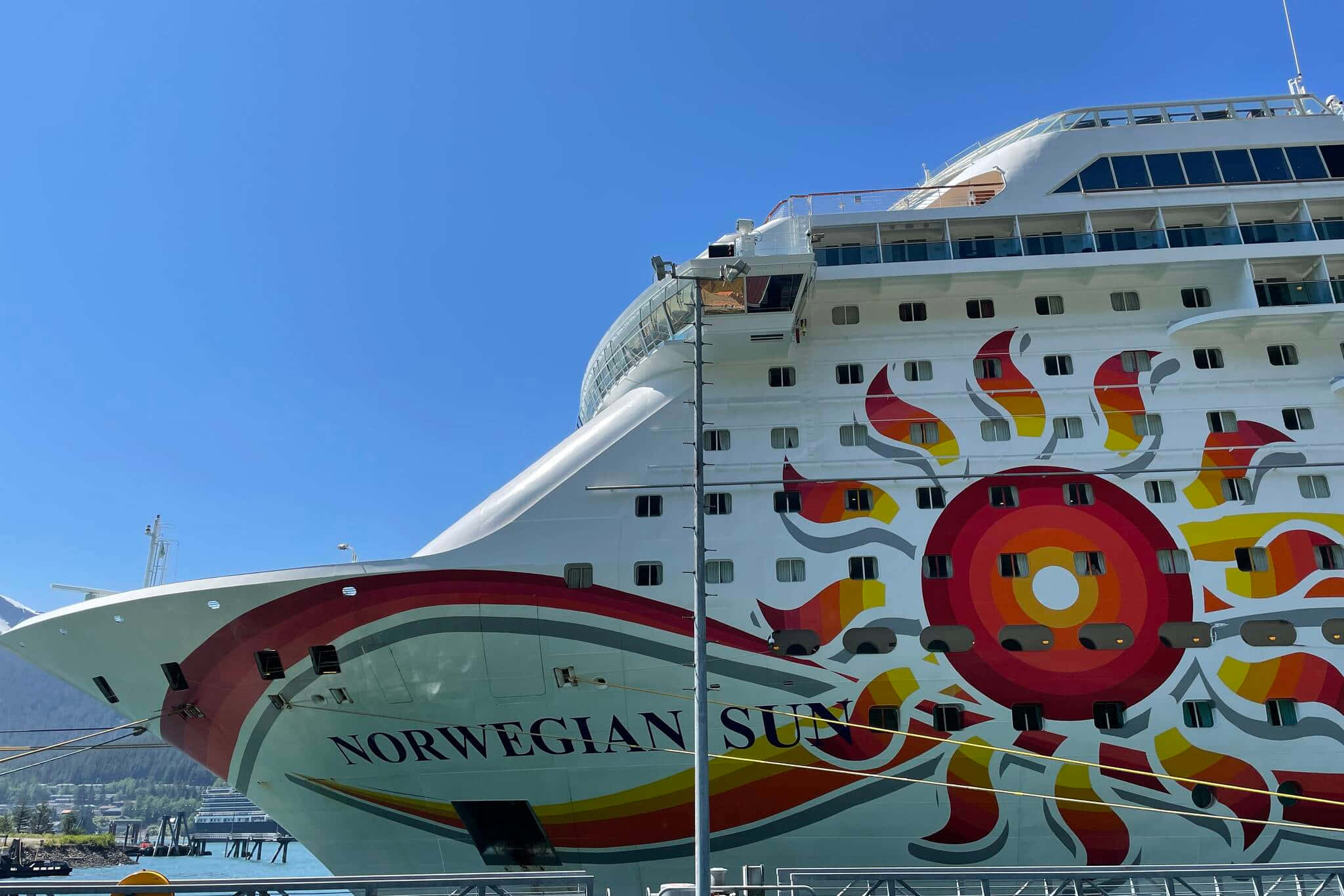 郵輪 桌布 壁紙 — 一艘名為 Norwegian Sun 的巨型白色郵輪，帶有鮮豔的紅橙色太陽爆發壁畫，在清澈的藍天下佔據了畫面主導地位。