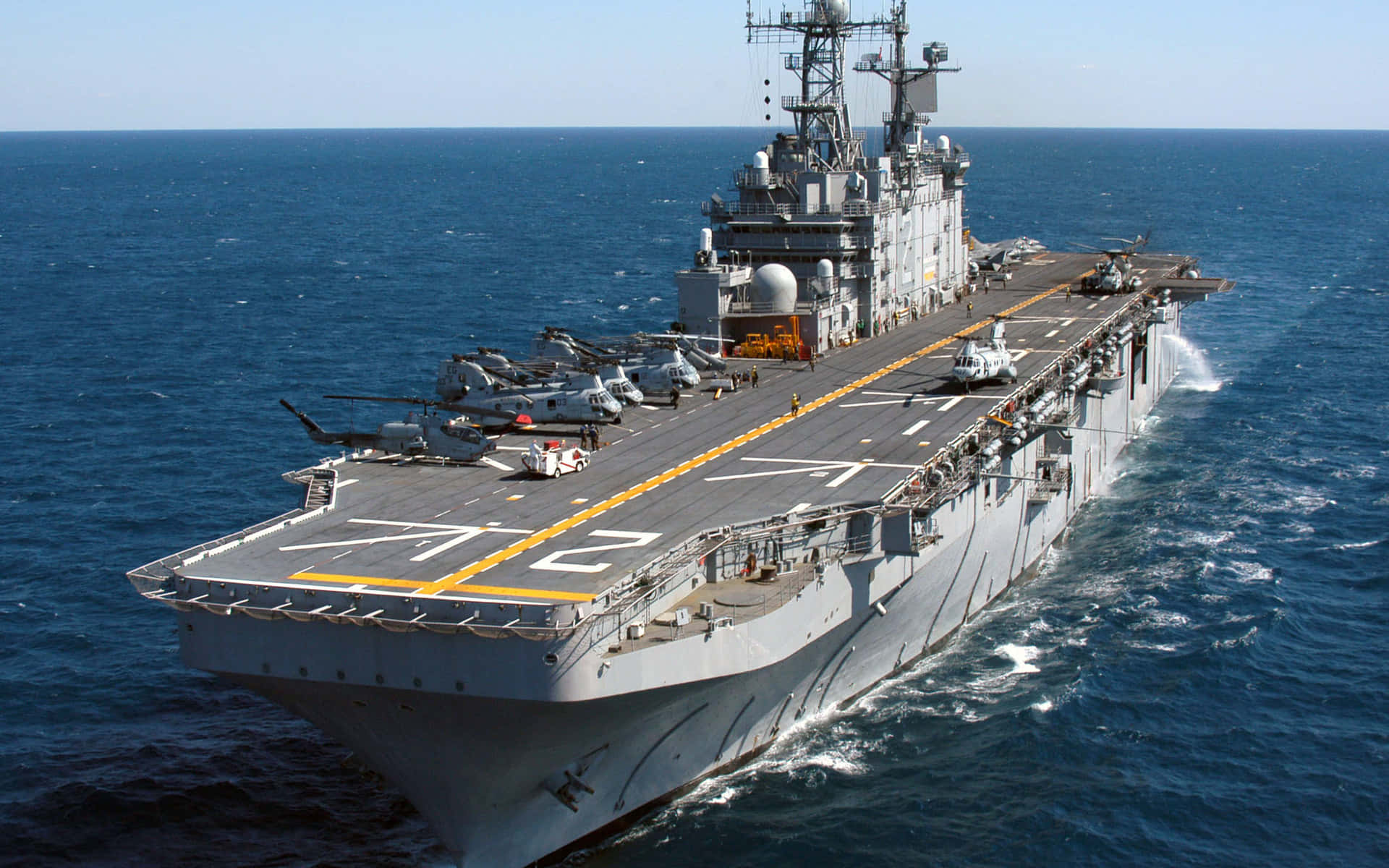 Navy 桌布 壁紙 — 一艘大型灰色航空母艦在深藍色海洋中航行，飛行甲板上停有直升機。