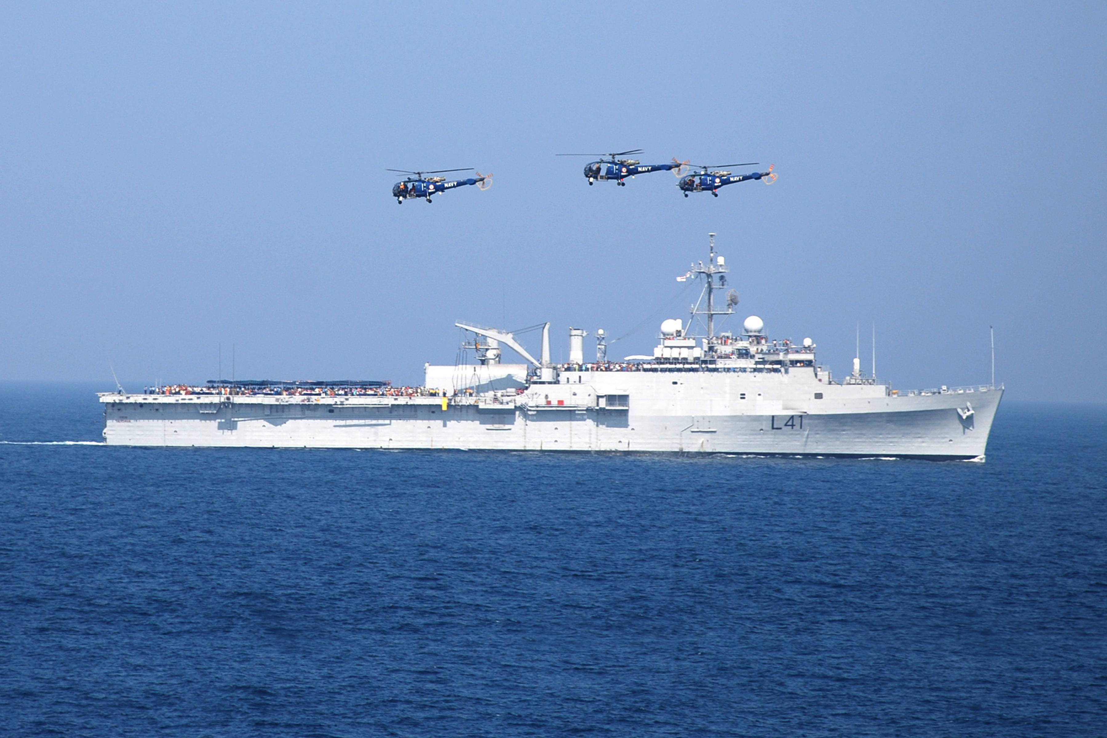 Warship 桌布 壁紙 — 一艘大型灰色軍艦在深藍色海洋上航行，三架直升機在晴朗天空下以編隊飛行。