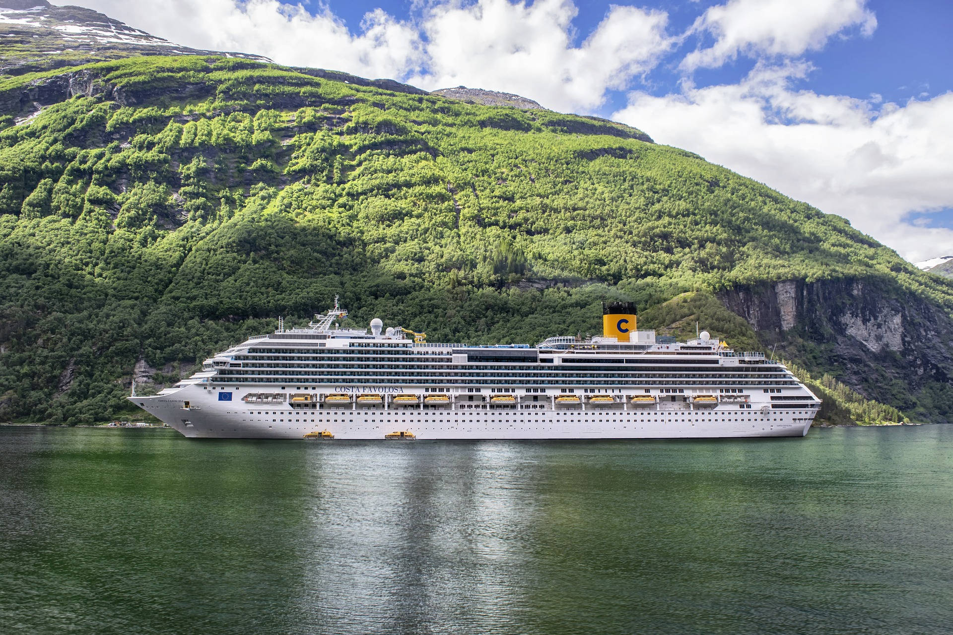 Norway 桌布 壁紙 — 一艘大型白色郵輪平靜地航行在深綠色的峽灣中，兩旁是高聳的翠綠山脈，上方是明亮的藍天和蓬鬆的白雲。