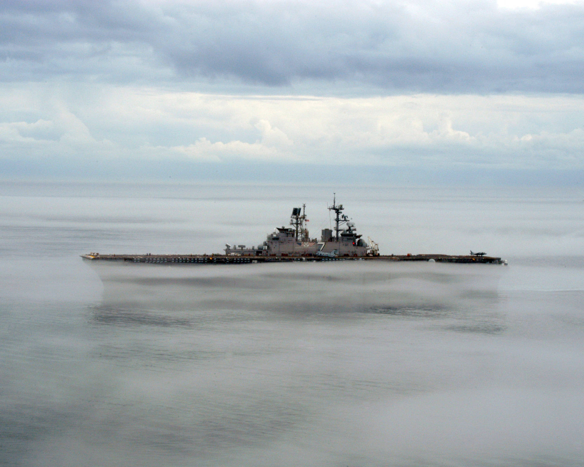 在多雲的天空下，一艘軍艦部分被海霧遮蔽。