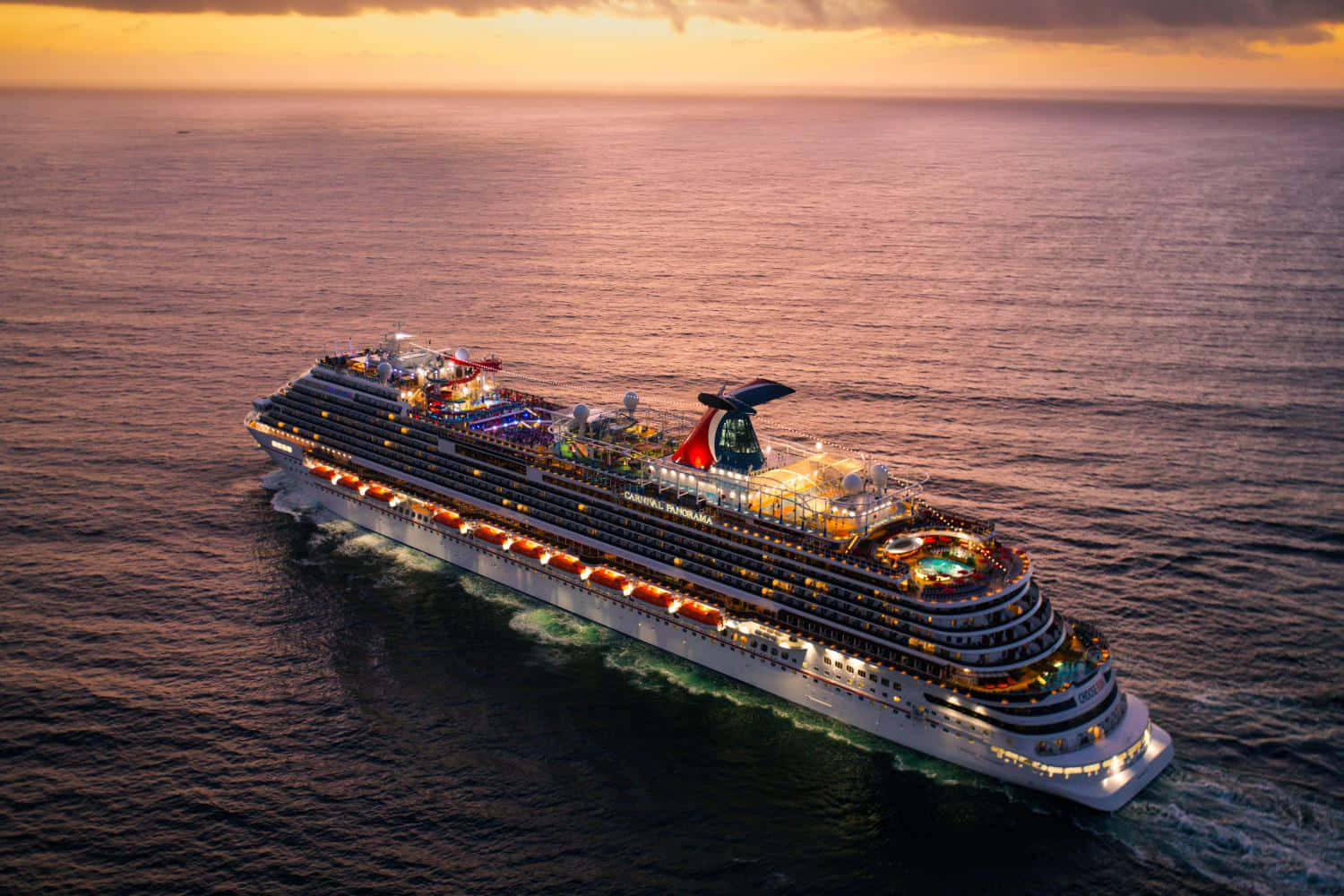 Carnival Conquest 桌布 壁紙 — 一艘大型郵輪在日落時分航行於平靜的海面上，甲板上溫暖的燈光閃爍。
