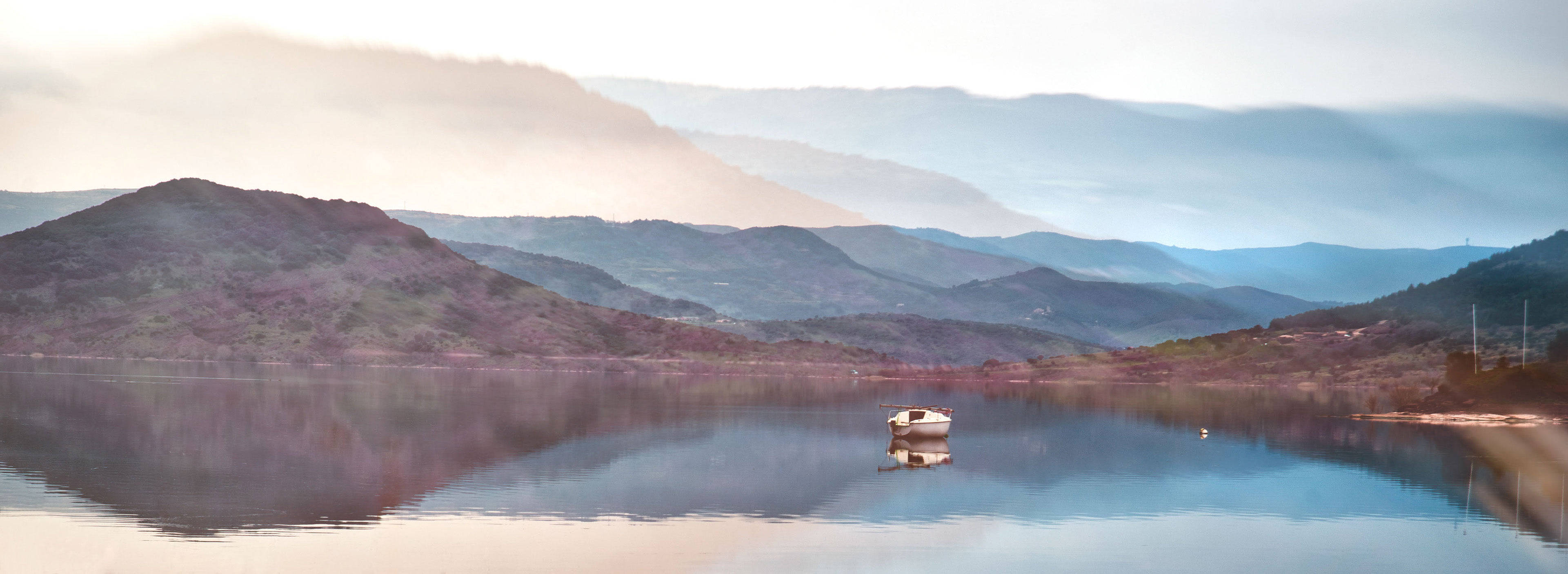 Calming 桌布 壁紙 — 一艘孤獨的小船靜靜地漂浮在平靜的湖面上，映照著薄霧籠罩的山巒，在柔和的黎明天空下。