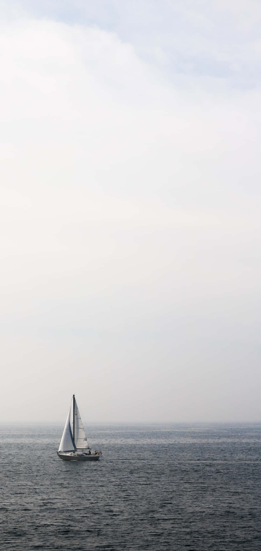 Sailboat 桌布 壁紙 — 一艘孤獨的帆船在平靜的灰色水面上滑行，頭頂是廣闊的多雲天空。
