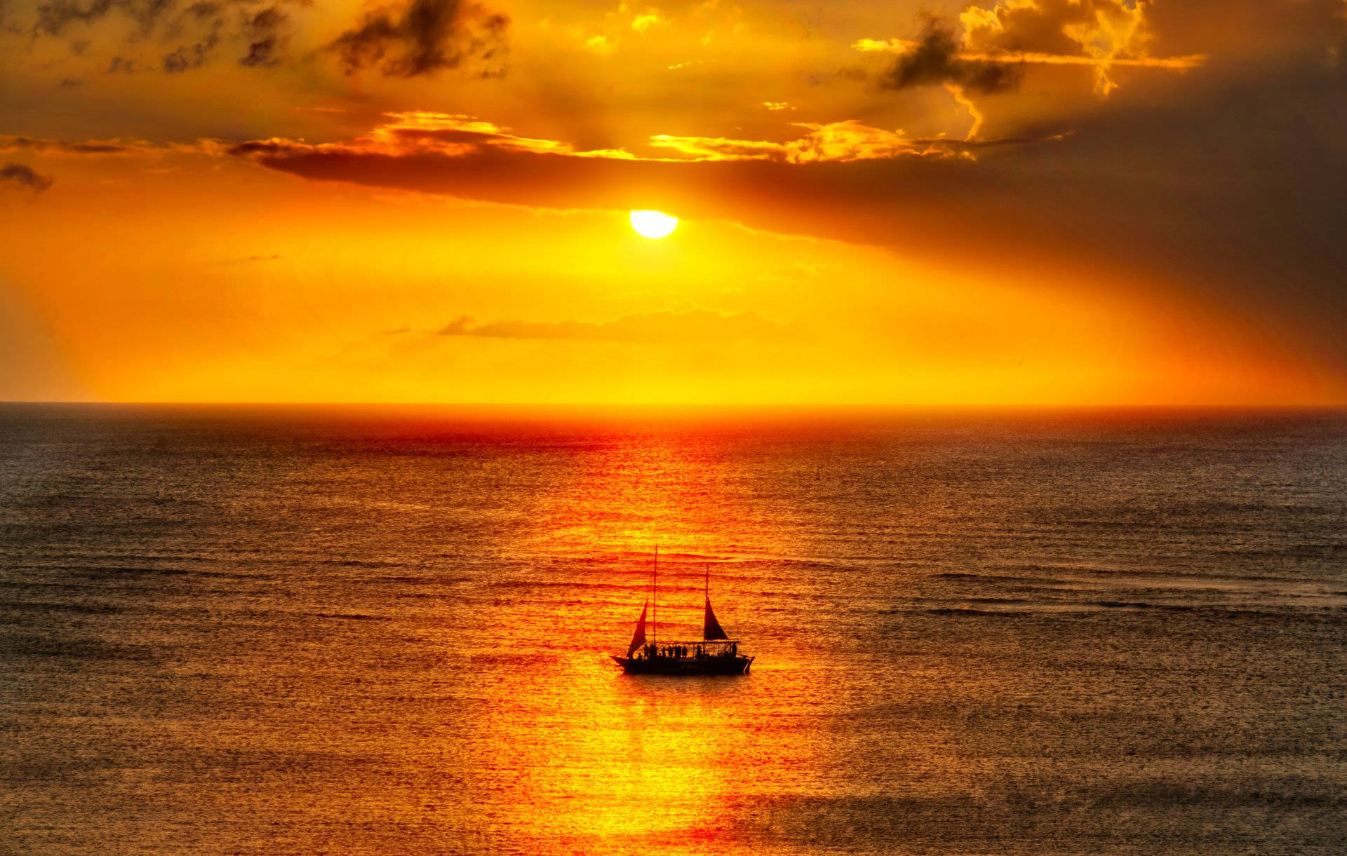 Caribbean 桌布 壁紙 — 一艘孤獨的帆船在廣闊的海洋上滑行，夕陽以火熱的橙色和金色色調落下。