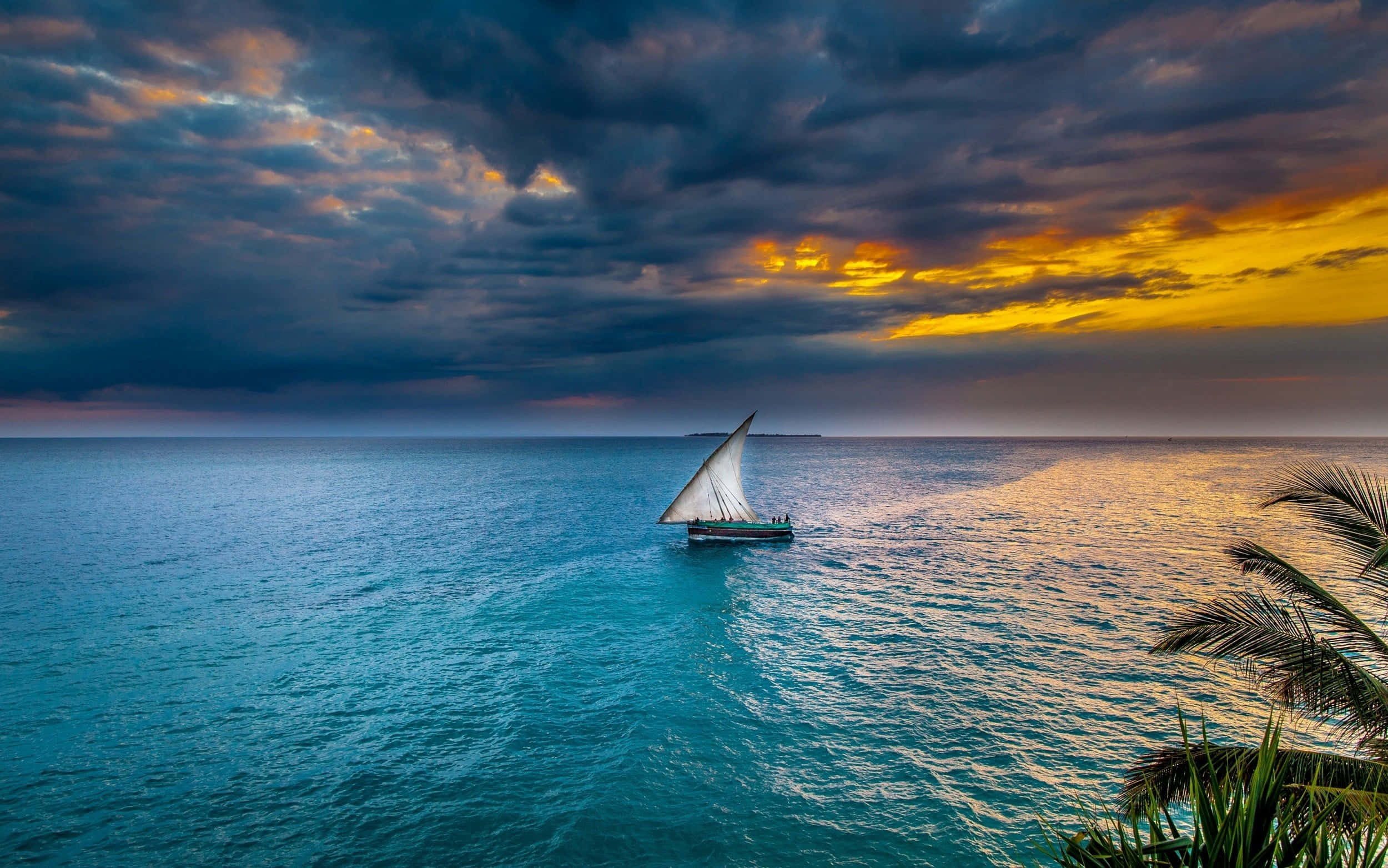 Sailboat 桌布 壁紙 — 一艘孤獨的帆船在碧綠色的海面上滑行，天空是戲劇性的日落，金色雲朵和黑暗的暴風雲籠罩著。