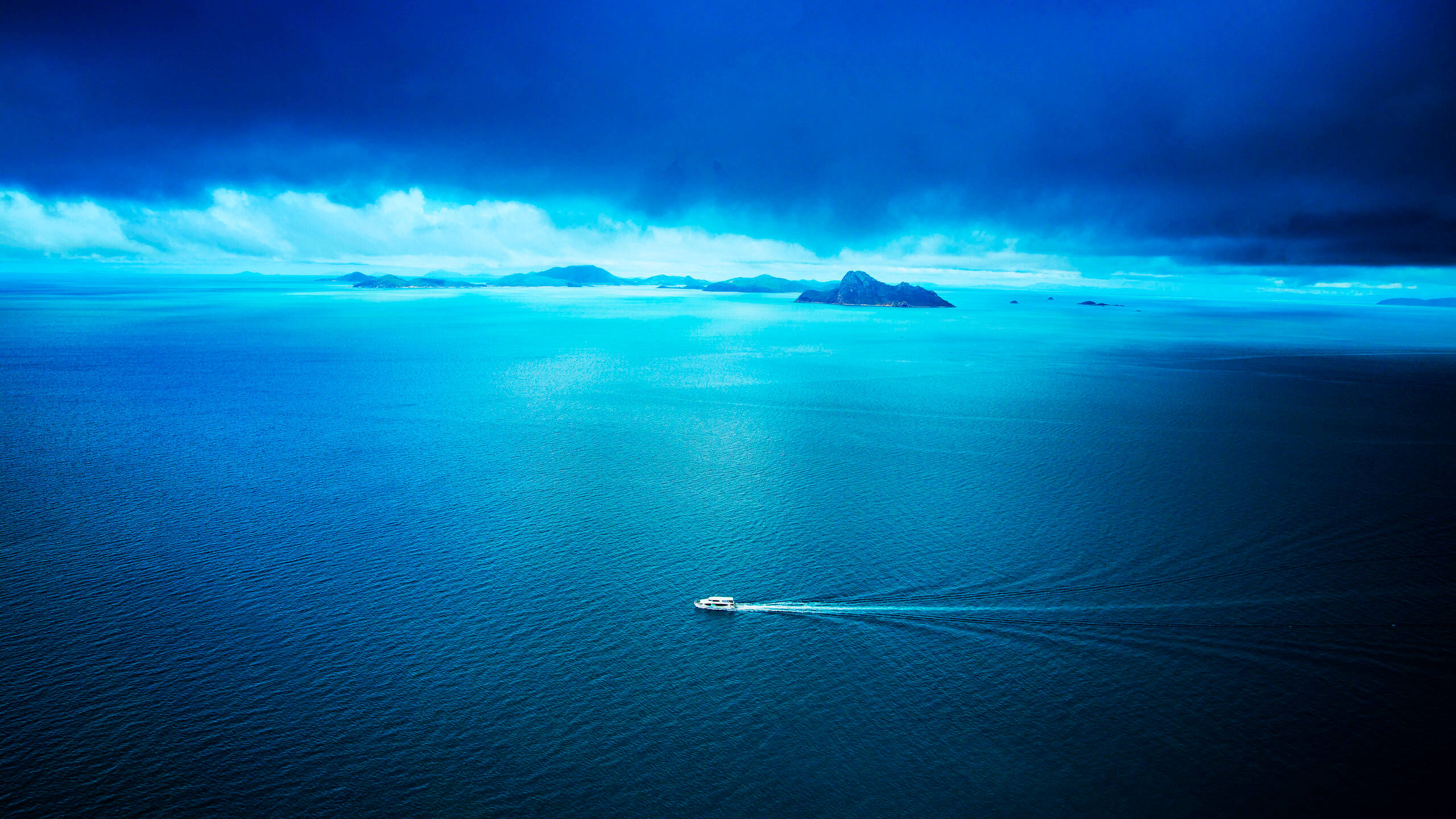 Boat 桌布 壁紙 — 一艘孤獨的快艇在廣闊的碧綠海水中破浪前行，天空戲劇性地風起雲湧，遠方島嶼隱現。