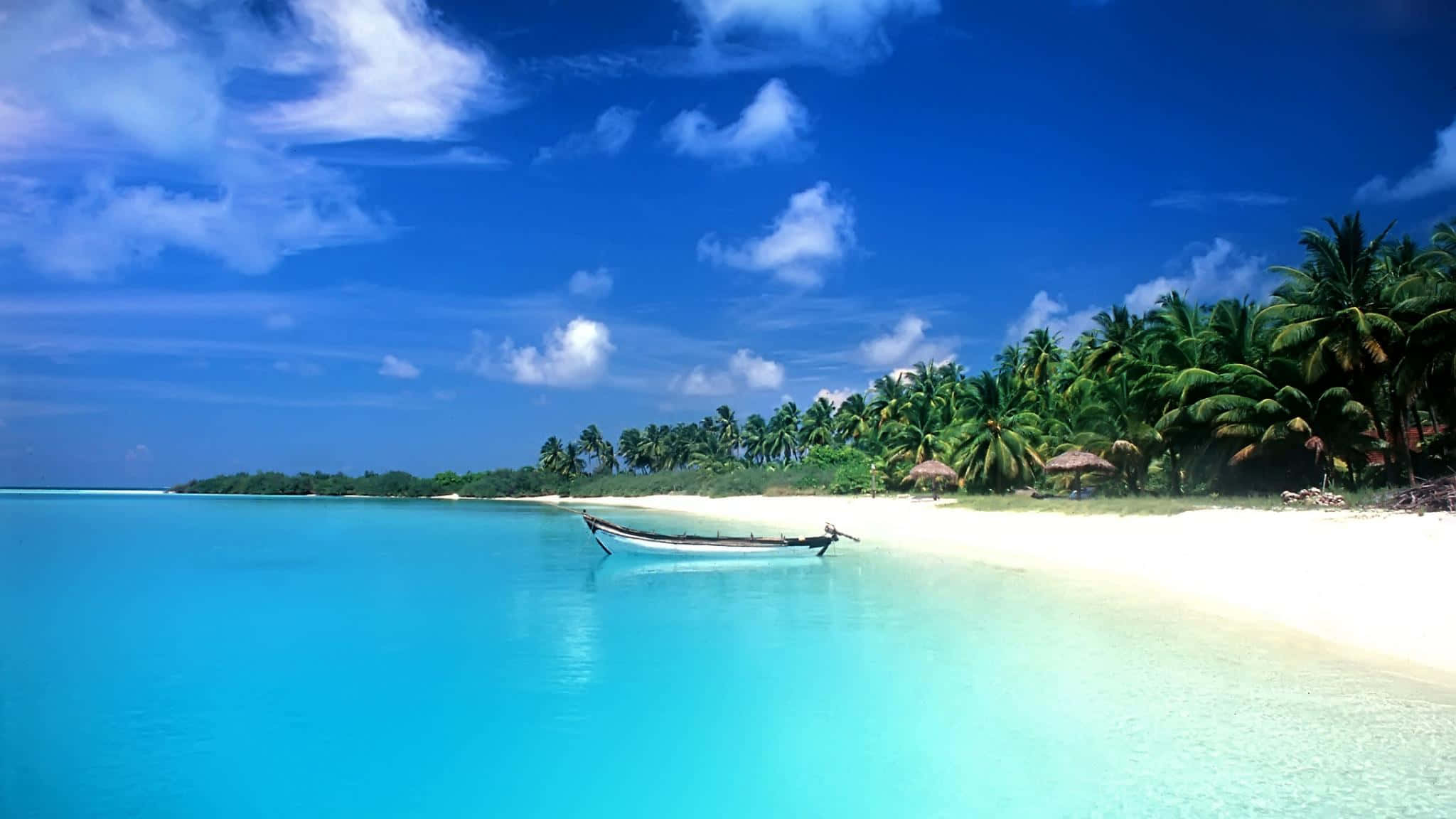 Beautiful Beach 桌布 壁紙 — 一艘孤獨的木船停泊在 pristine 白色沙灘旁，旁邊是碧綠的海水，上方是湛藍的天空，點綴著幾朵雲彩。