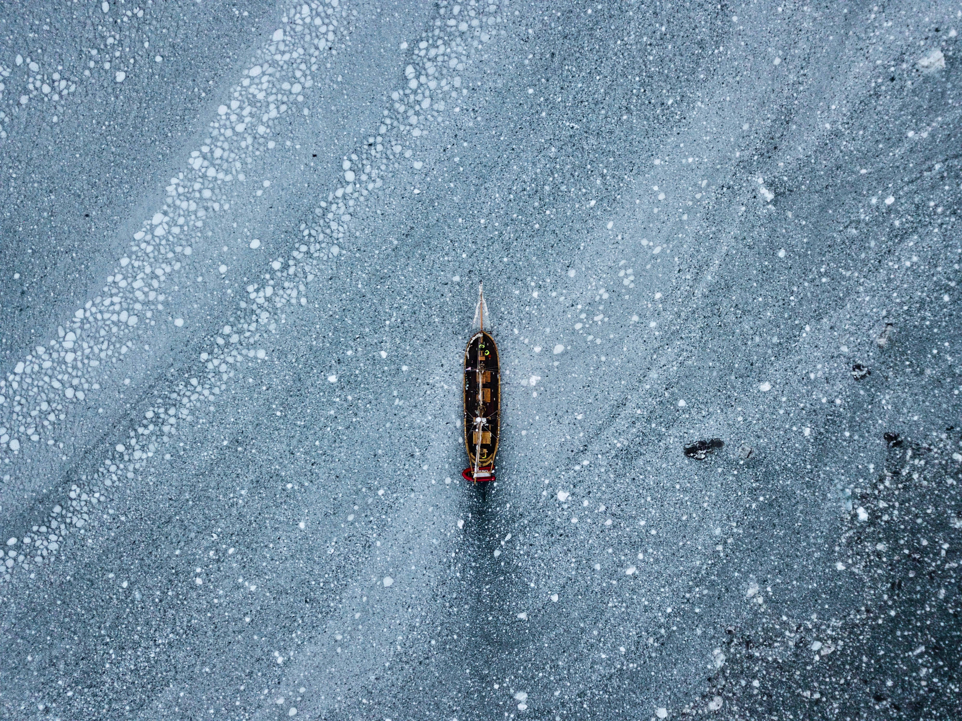 Greenland 桌布 壁紙 — 一艘孤獨的木船停泊在廣闊的冰凍湖中央，周圍有複雜的冰紋向外輻射。