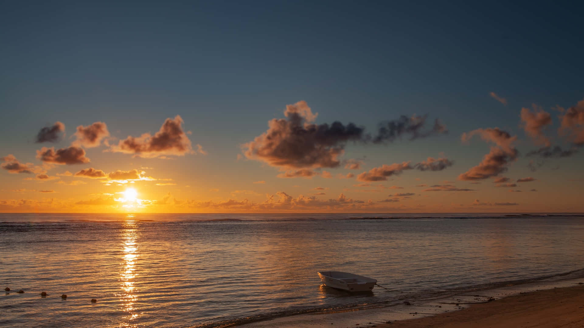 1920x1080 HD Beach 桌布 壁紙 — 一艘孤獨的白色小船停泊在沙灘上，夕陽在平靜的海面上落下，將金色的光芒灑向天空和水面。