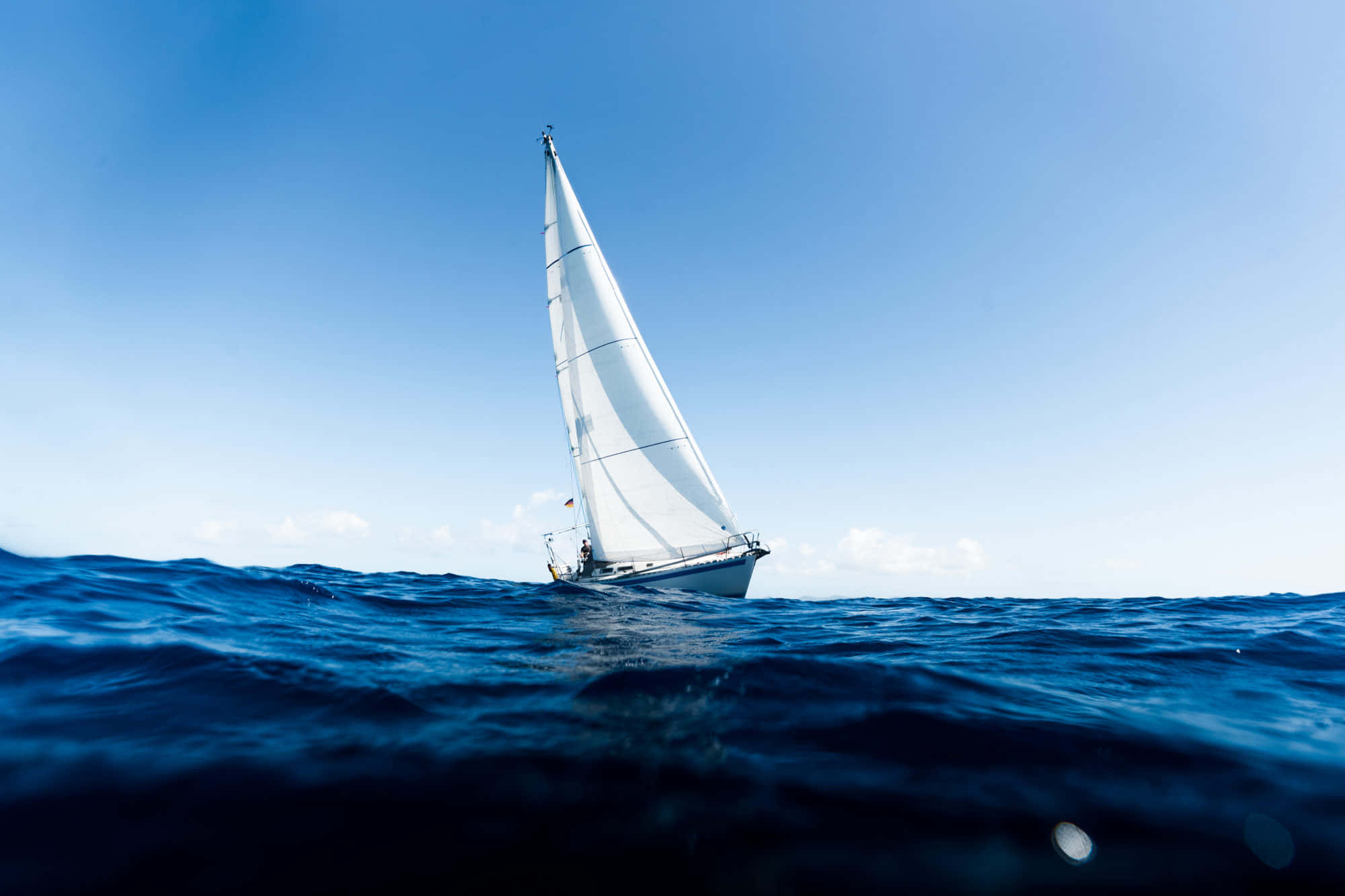 Sailboat 桌布 壁紙 — 一艘孤獨的白色帆船在晴朗的天空下滑過深藍色的海浪。
