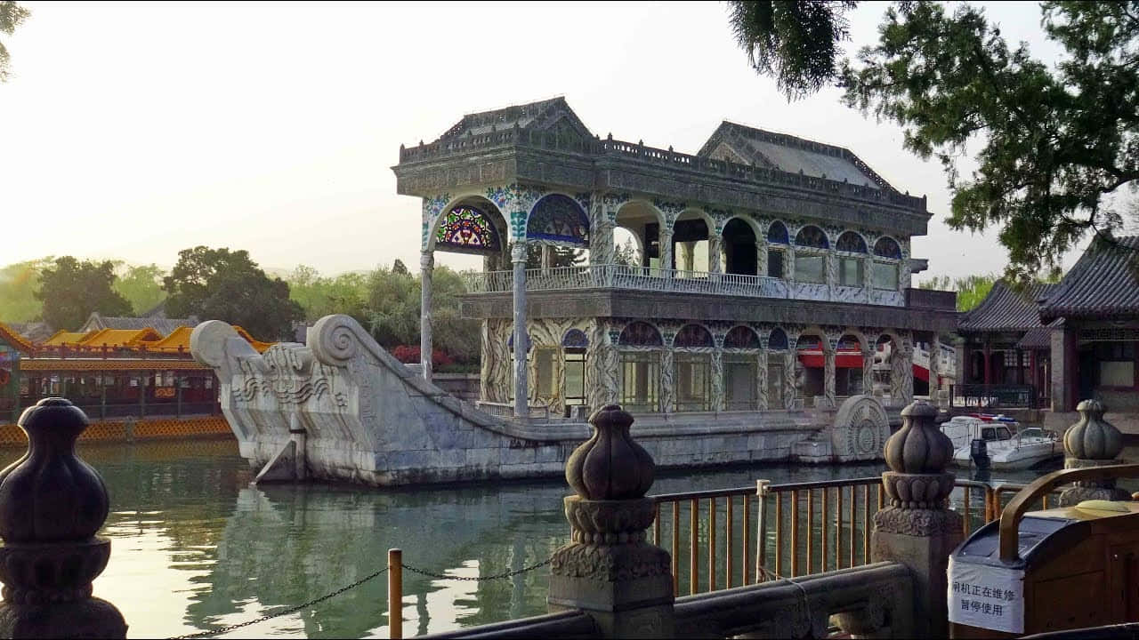 船 桌布 壁紙 — 一艘宏偉華麗的石舫，雕刻精細，在平靜的水面上悠然漂浮，四周環繞著傳統中式建築和茂密的綠樹。
