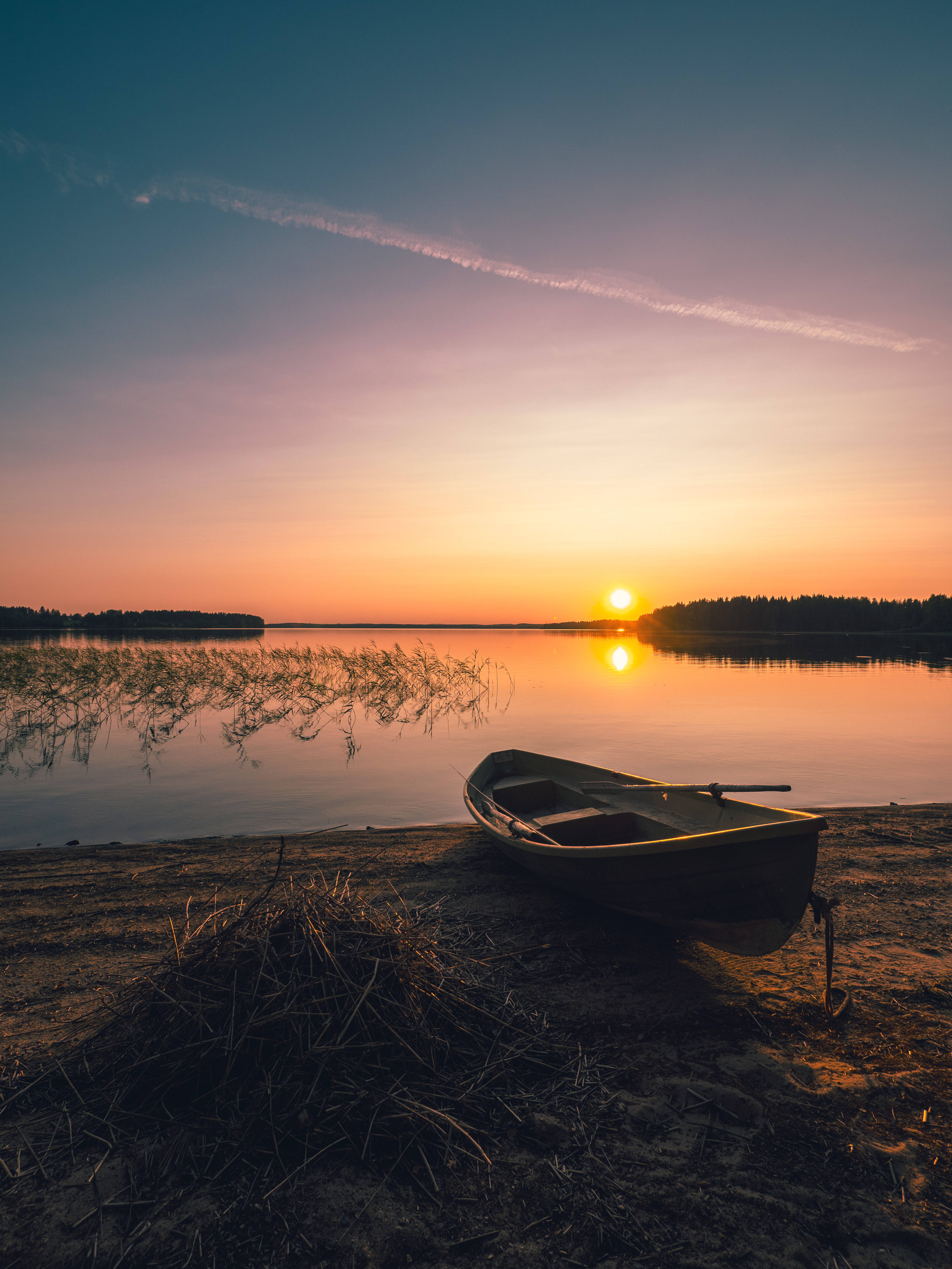 Finland 桌布 壁紙 — 一艘小船停泊在沙灘上，夕陽落在平靜的湖面上，反射出溫暖的橙色和紫色色調。