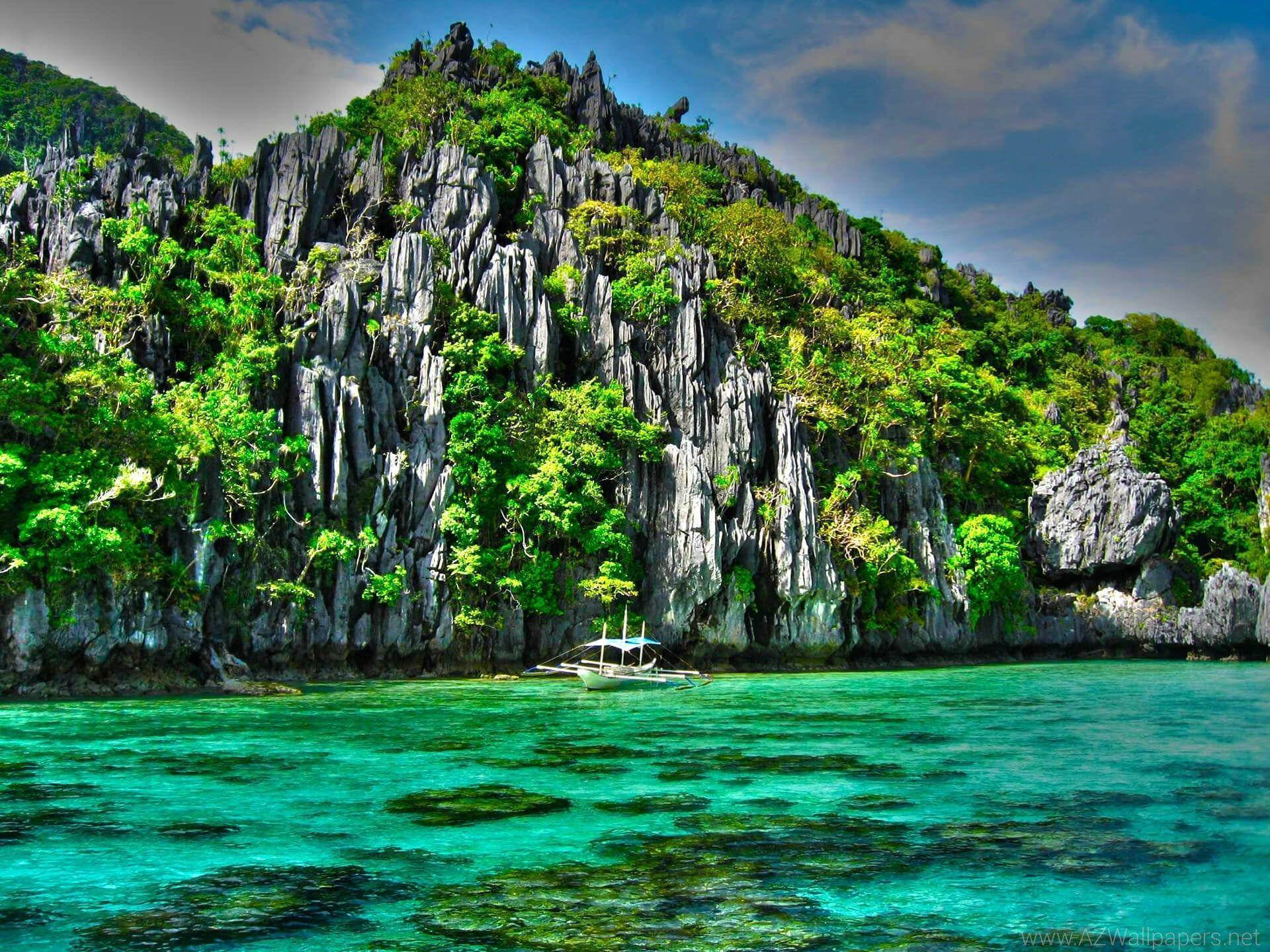 Philippines 桌布 壁紙 — 一艘小船漂浮在充滿活力的碧綠海水上，前方是雄偉的石灰岩懸崖，覆蓋著茂密的綠色植物，天空部分多雲。
