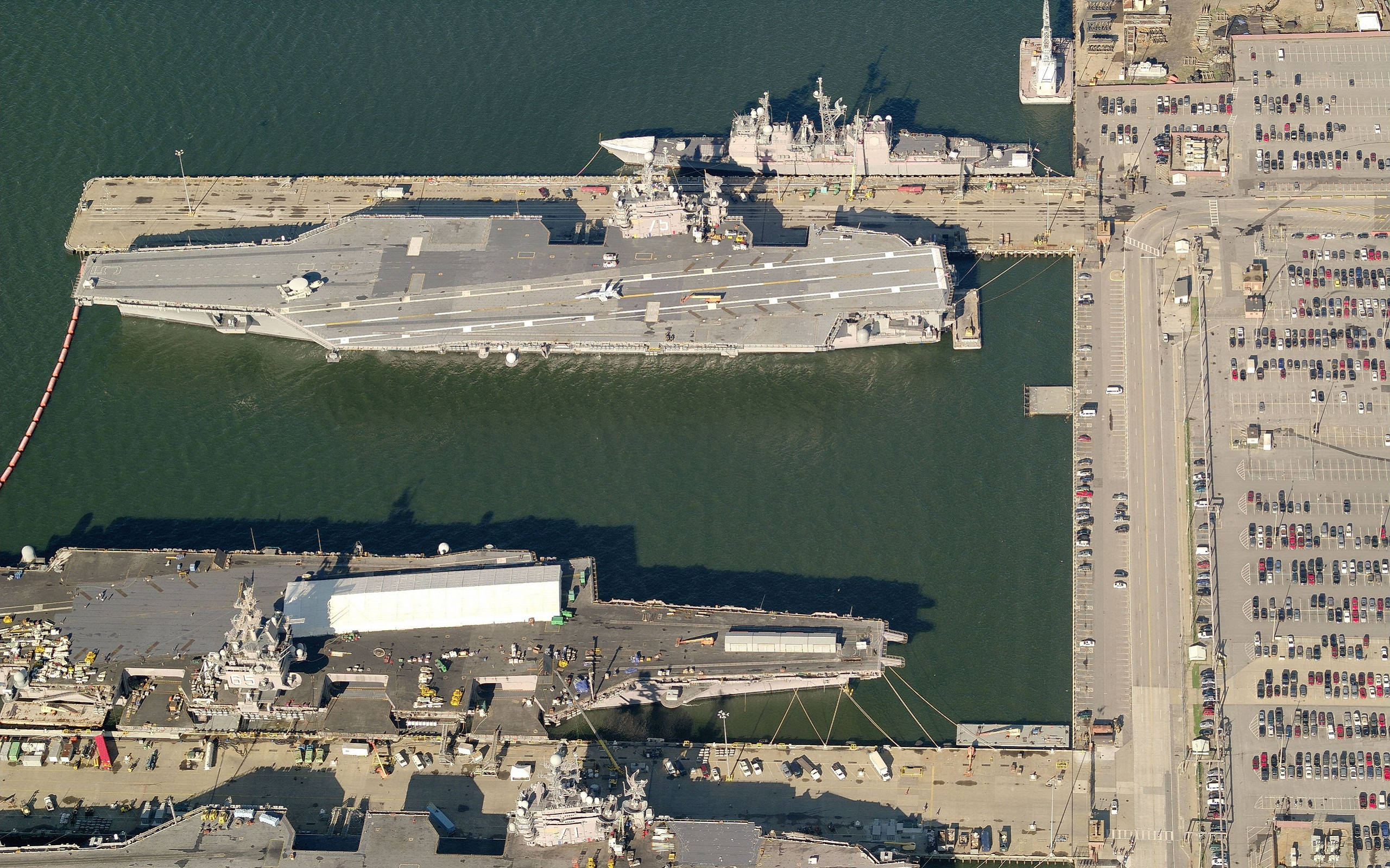 Warship 桌布 壁紙 — 一艘巨型航空母艦停泊在一個海軍基地的鳥瞰圖，周圍有停車場和工業建築。