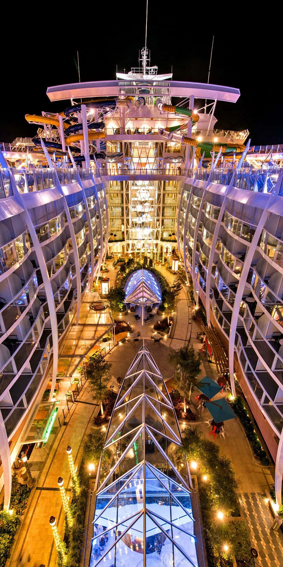 Cruise 桌布 壁紙 — 一艘巨大照明郵輪的夜間空中景觀，設有發光甲板、水上滑梯和中央中庭。