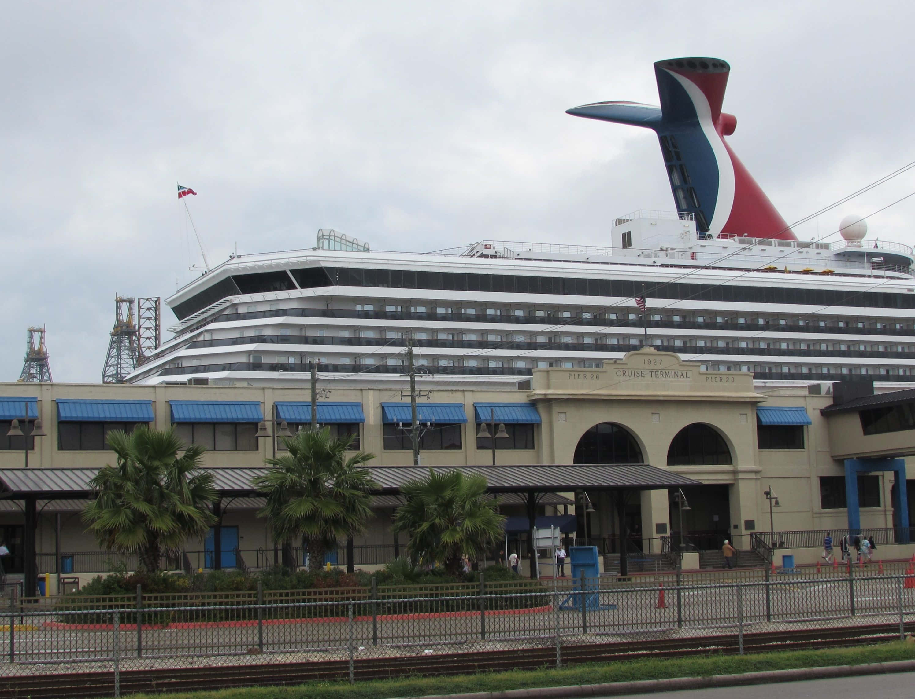 Carnival Dream 桌布 壁紙 — 一艘巨大的嘉年華郵輪在陰天之下聳立於歷史悠久的郵輪碼頭，前景有棕櫚樹和鐵軌。