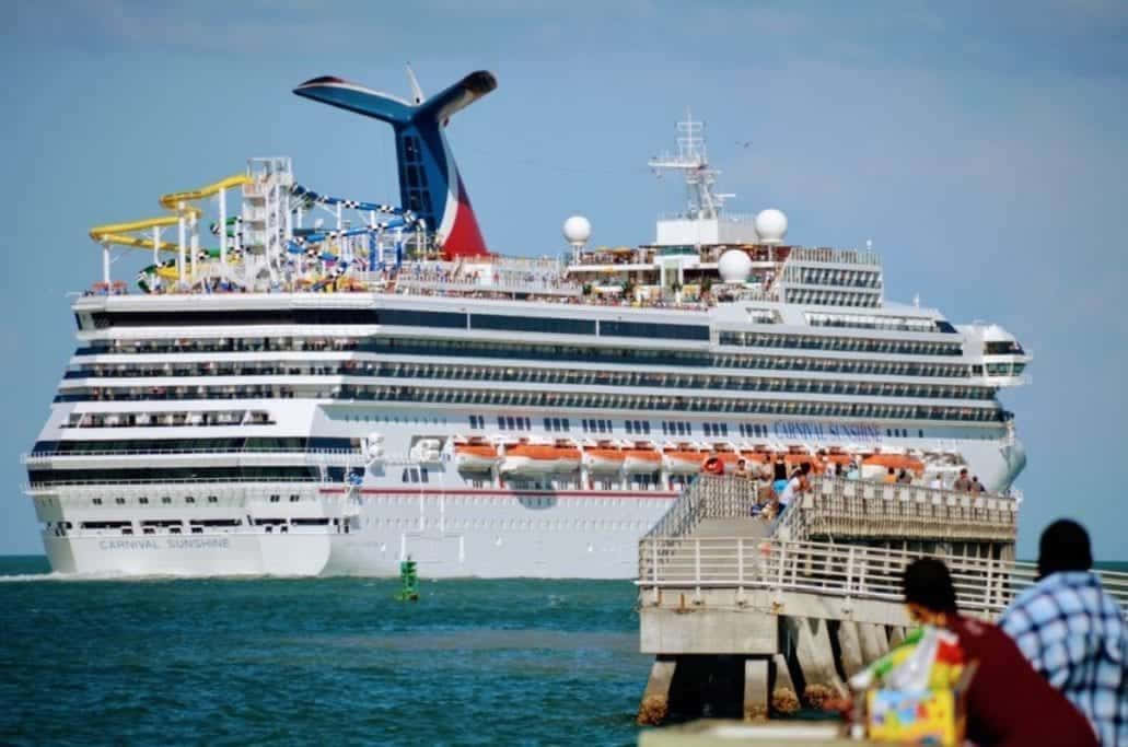 Cruise 桌布 壁紙 — 一艘巨大的嘉年華陽光號郵輪停靠在碼頭，人們在晴朗的藍天下從木板路上觀看。