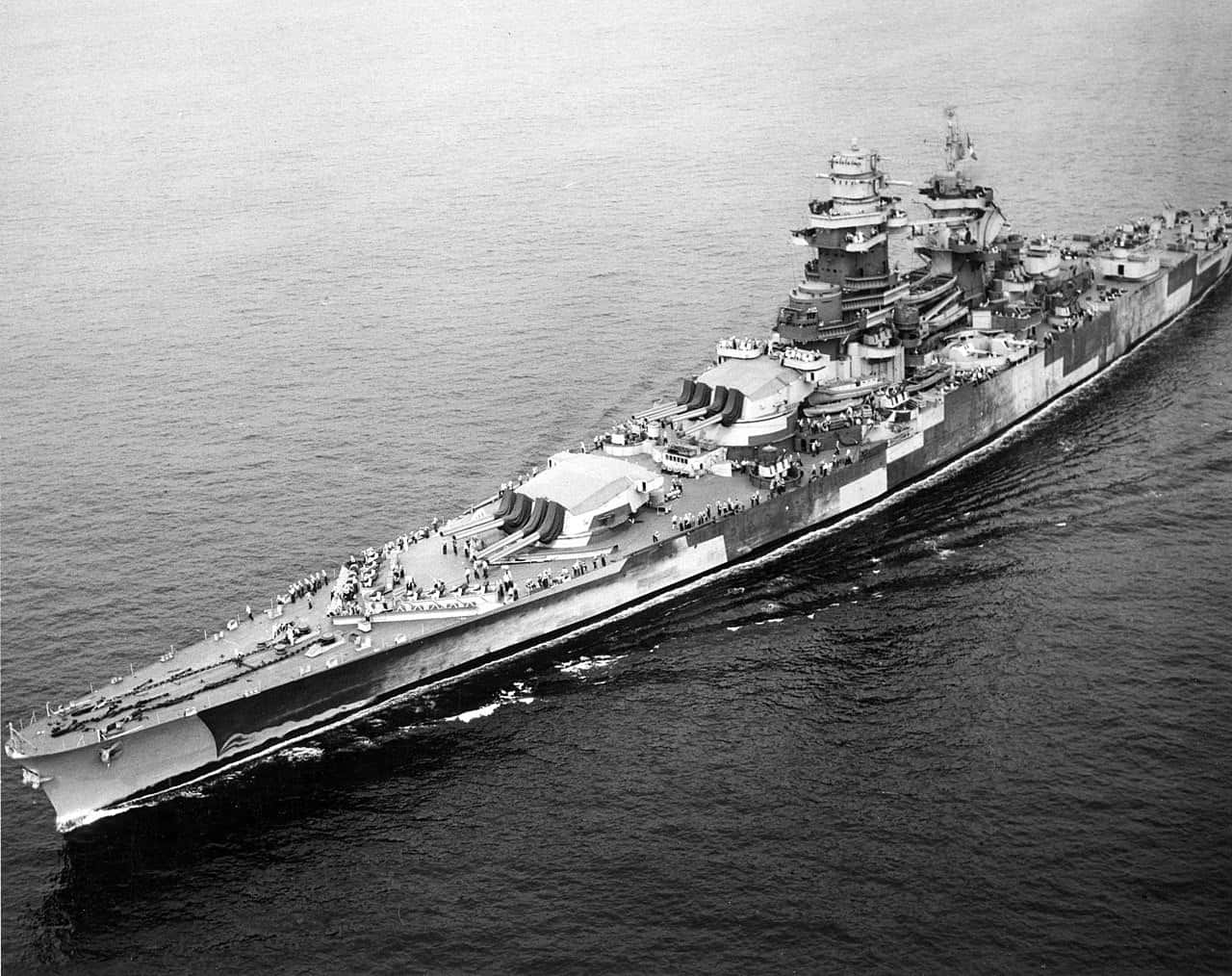 Battleships 桌布 壁紙 — 一艘巨大的戰艦在平靜的海面上航行，甲板上可見船員，呈現出引人注目的黑白航拍視角。