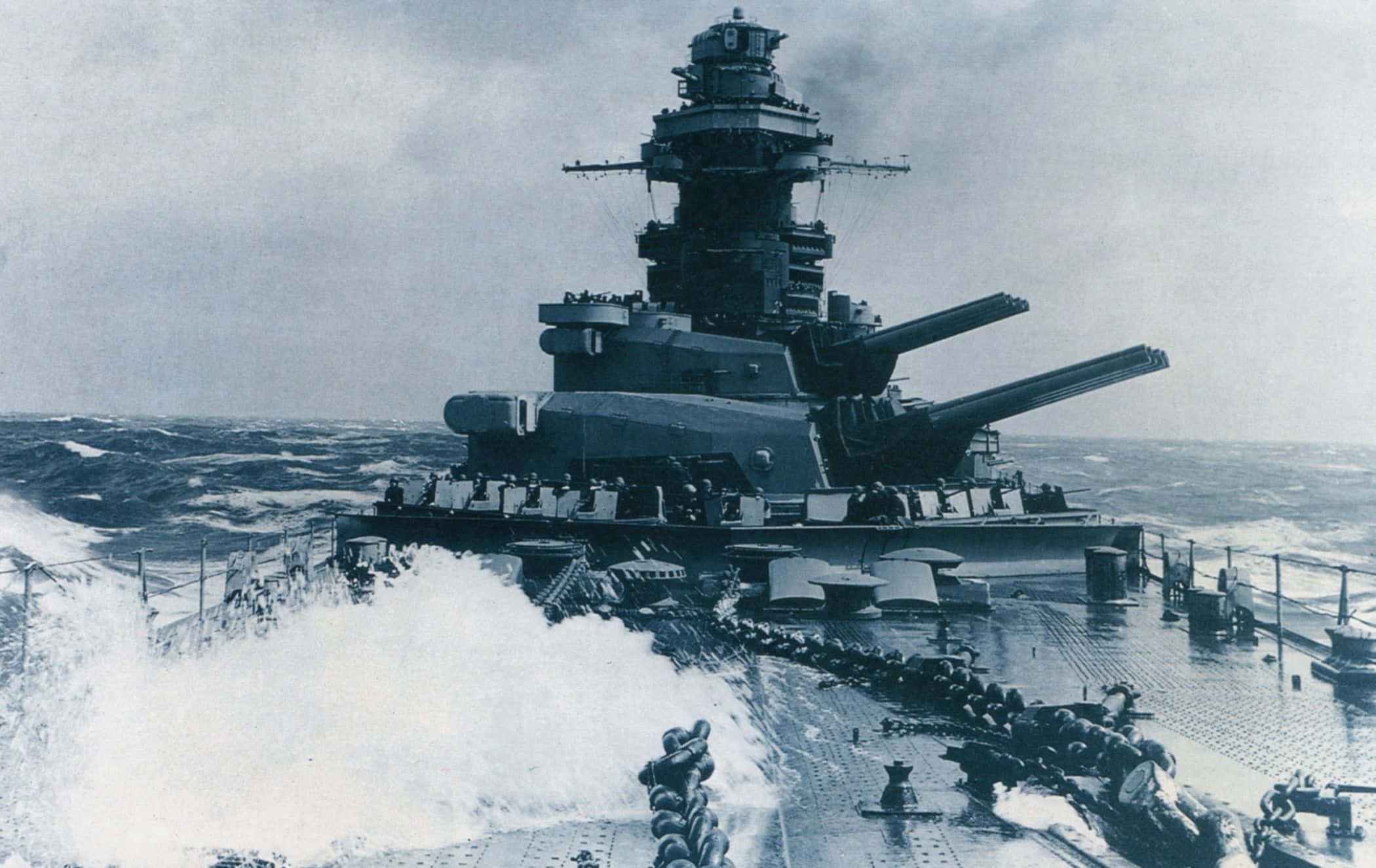 Battleship 桌布 壁紙 — 一艘巨大的戰艦在陰天中破浪前行，海浪拍打甲板。