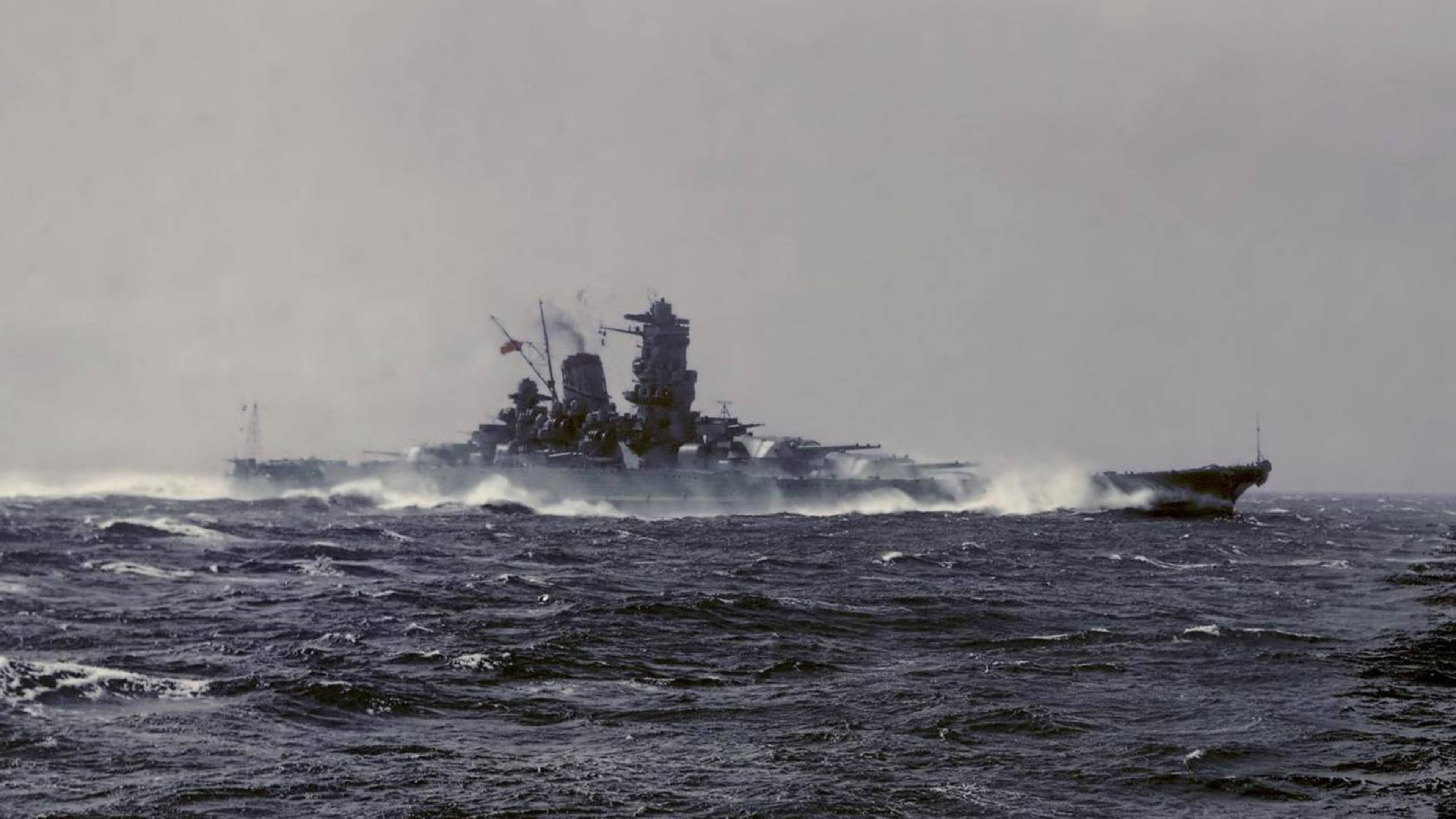 日式 桌布 壁紙 — 一艘巨大的戰艦在陰天之下劃過波濤洶湧的黑暗海水，留下泡沫般的尾跡。
