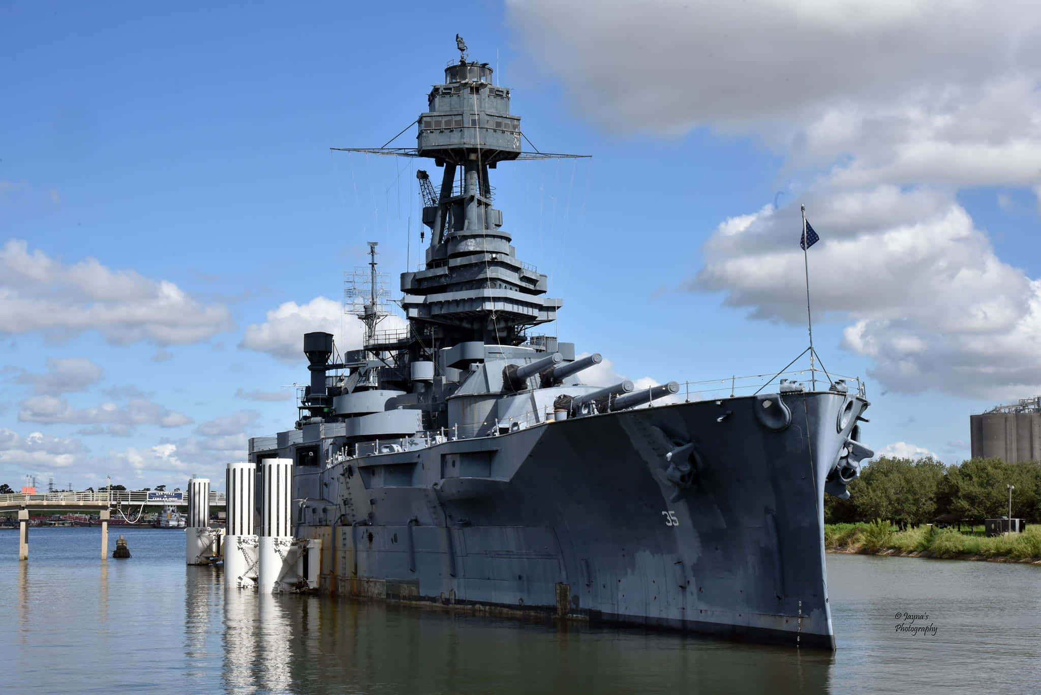 Battleships 桌布 壁紙 — 一艘巨大的灰色戰艦，擁有高聳的砲塔，停泊在平靜的水面上，天空多雲間晴。