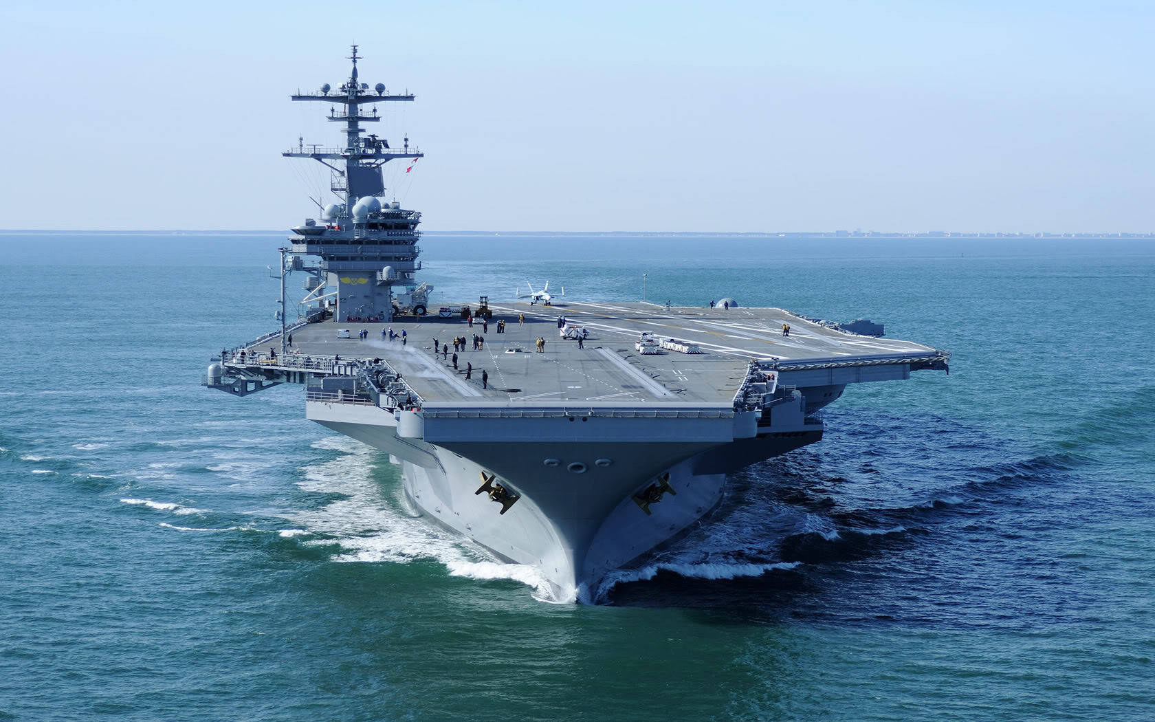 Warship 桌布 壁紙 — 一艘巨大的灰色航空母艦在晴朗的天空下劃過深藍色的海水，留下白色的尾跡。