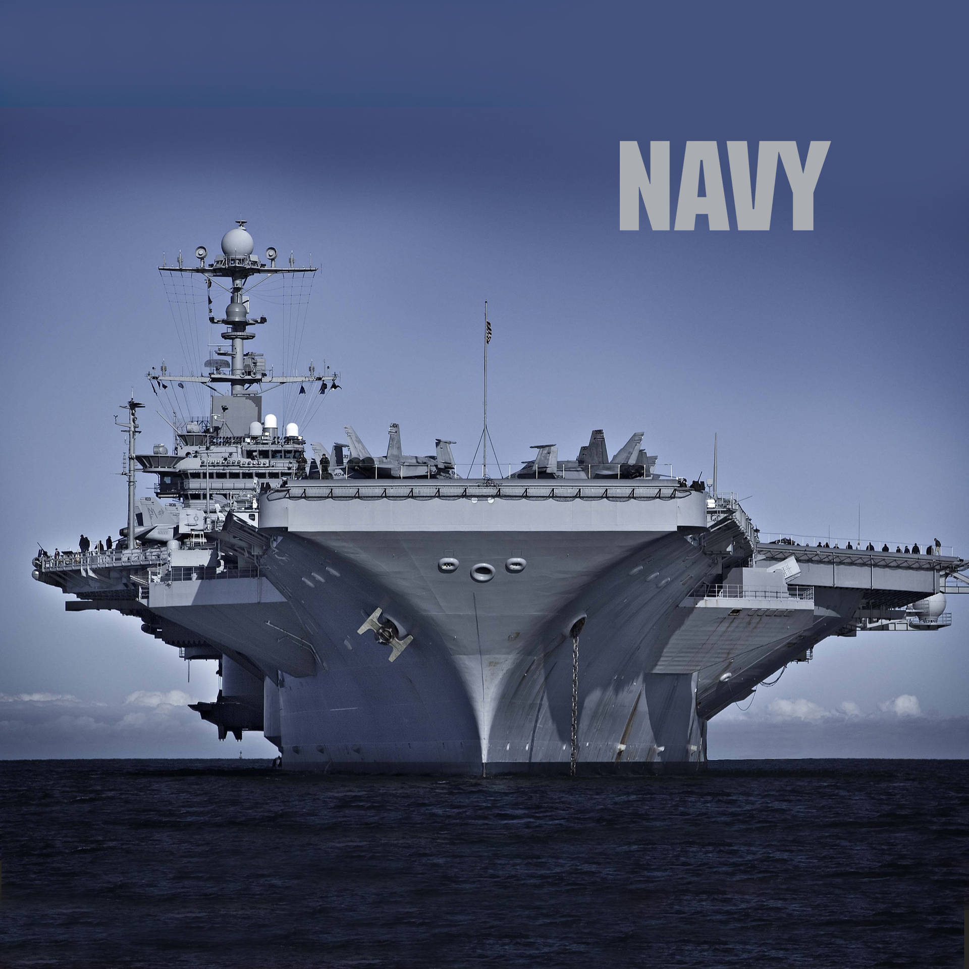 一艘大型灰色海軍航空母艦在海洋上航行，上方有「NAVY」文字。