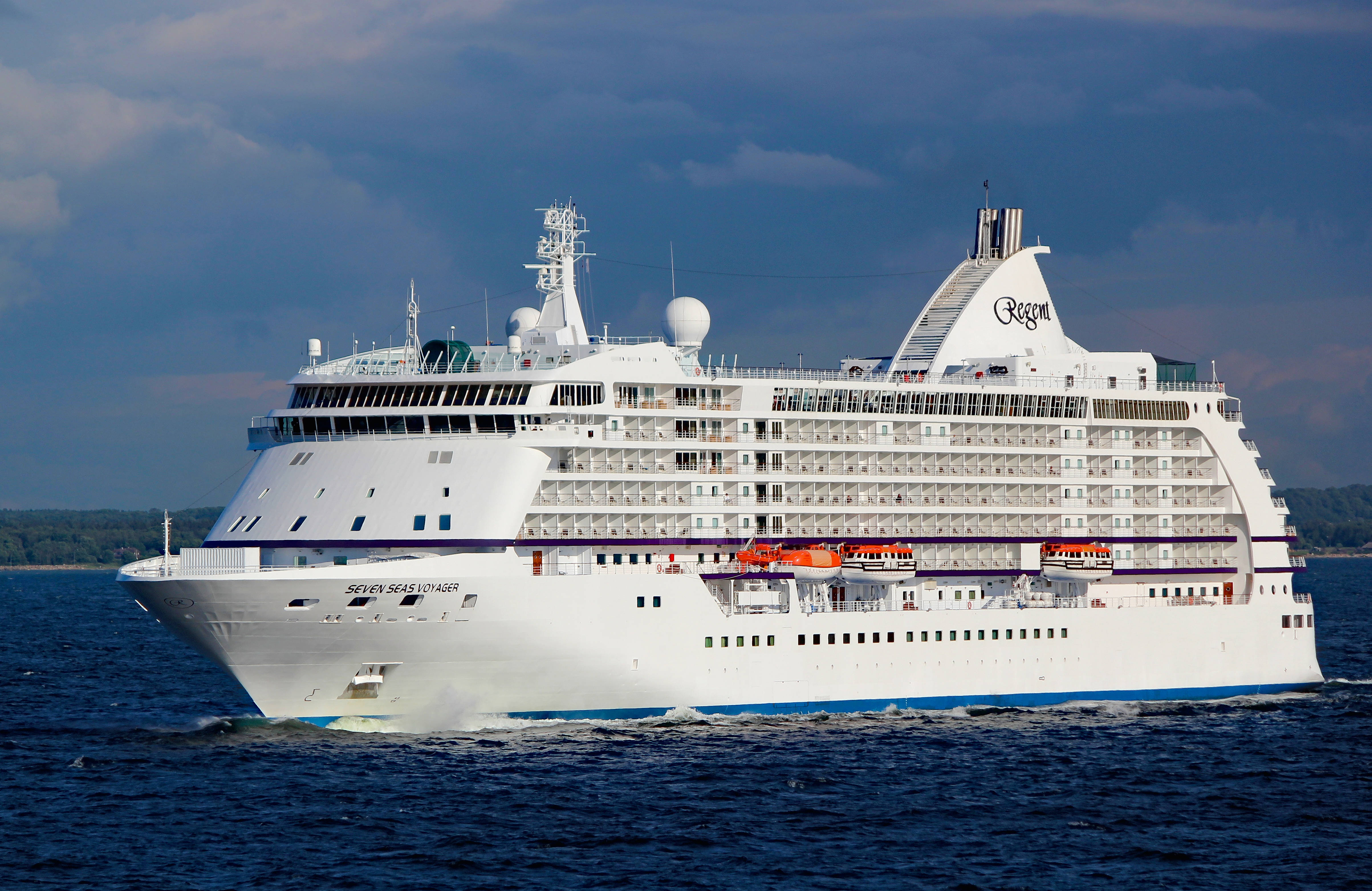 郵輪 桌布 壁紙 — 一艘巨大的白色Regent Seven Seas Voyager郵輪在戲劇性的多雲天空下航行於深藍色的海洋中。