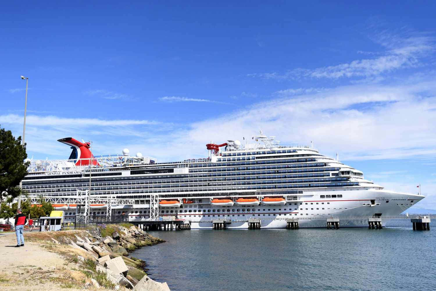Carnival Dream 桌布 壁紙 — 一艘巨大的白色嘉年華郵輪，帶有紅色煙囪，停泊在碼頭，天空湛藍，白雲點點。