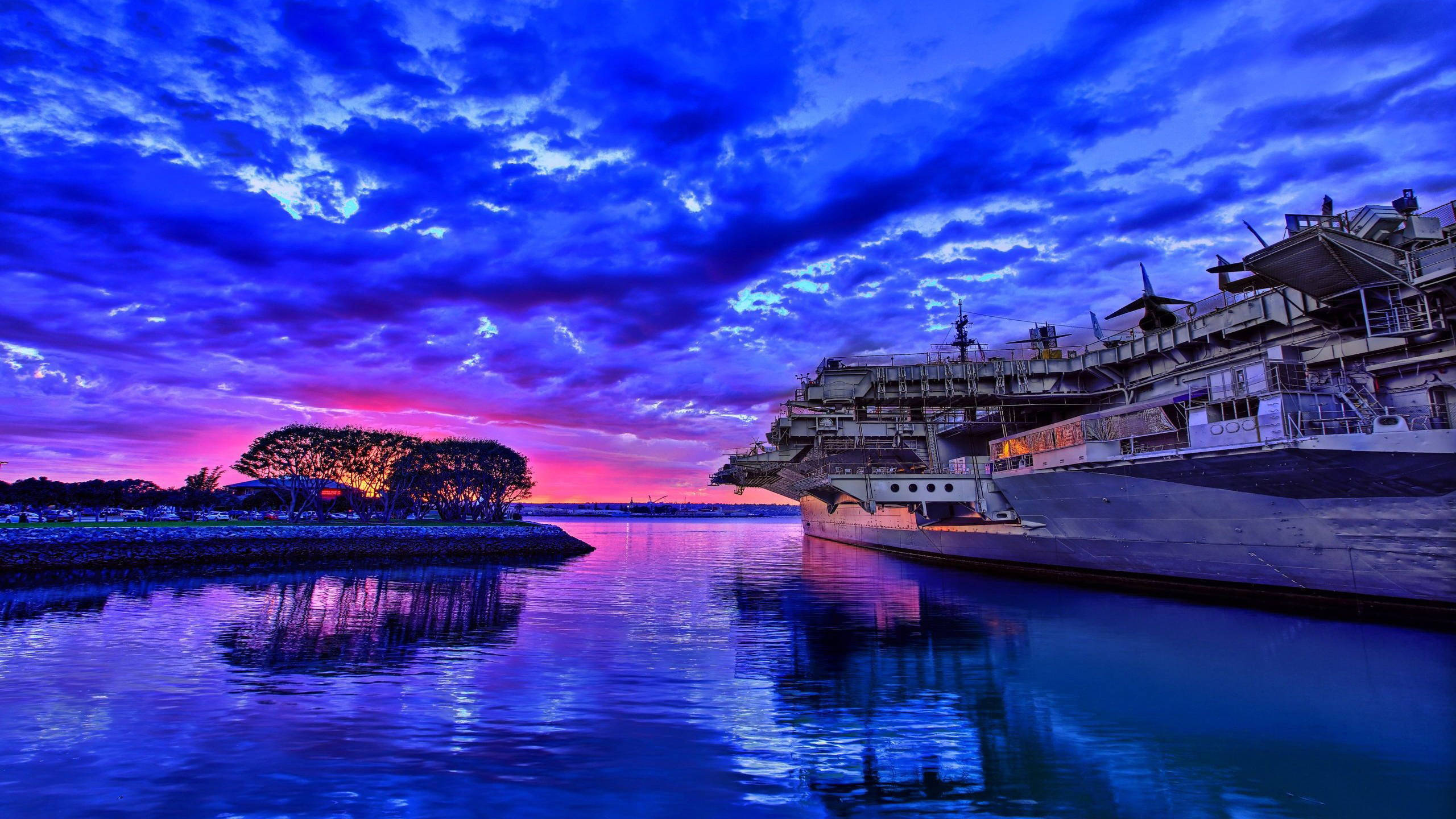Warship 桌布 壁紙 — 一艘巨大的航空母艦在平靜的水域中停泊，天空呈現戲劇性的暮色，塗滿了電光藍和火熱粉紅。