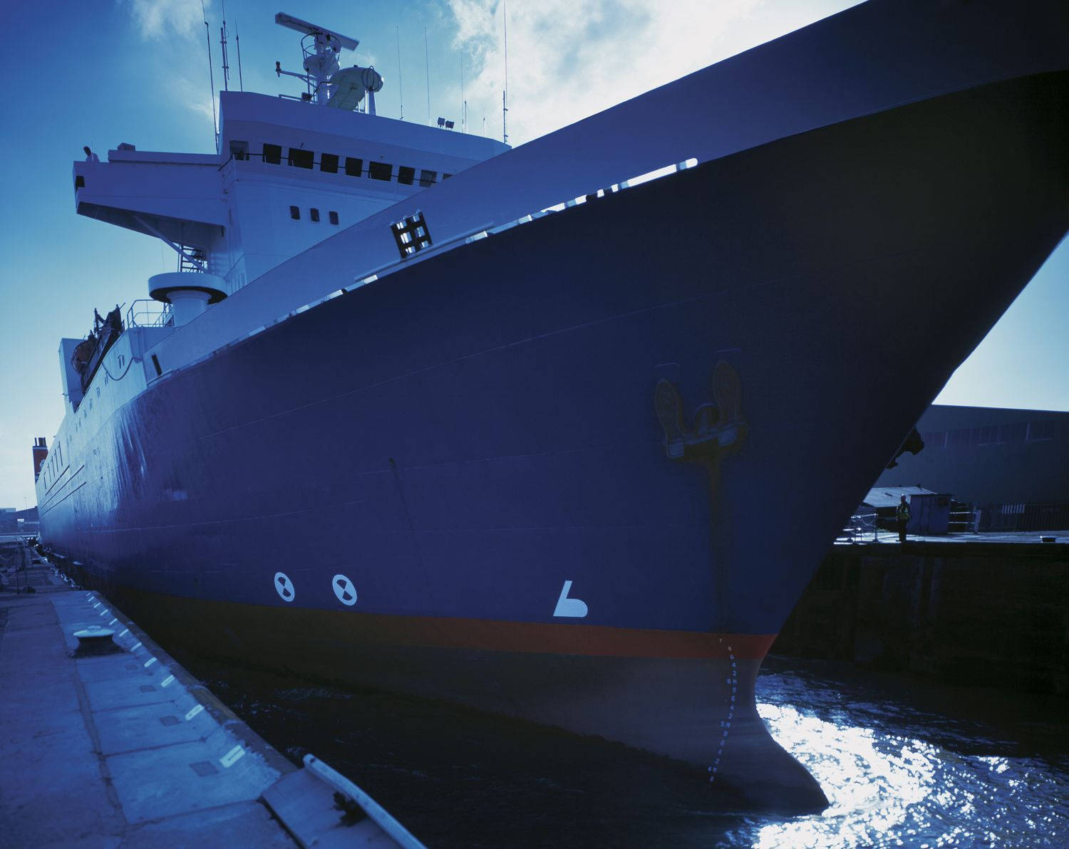 Boat 桌布 壁紙 — 一艘巨大的藍色船隻，帶有白色上層建築，在黎明時分停泊在港口，陽光在水面上閃爍。