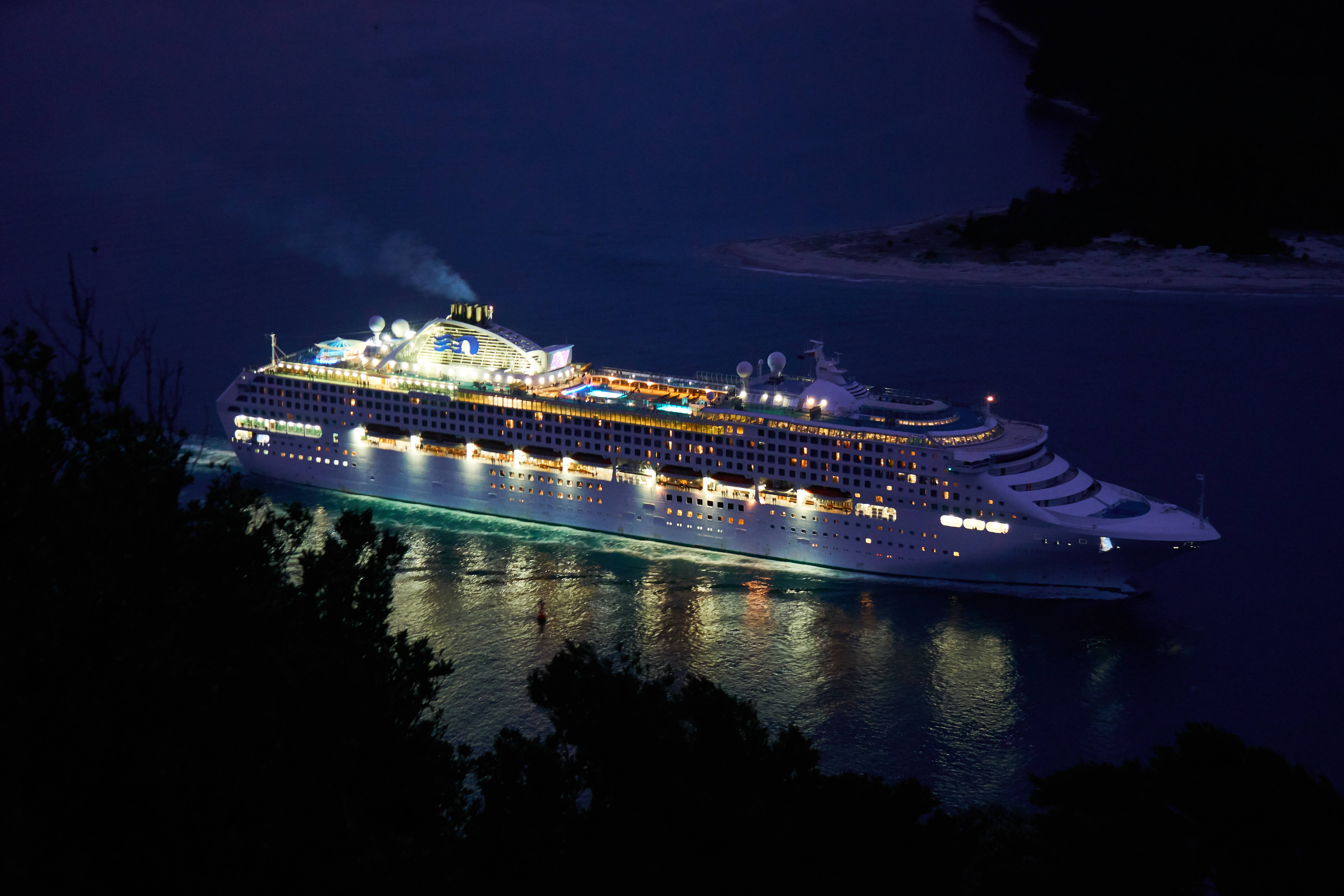 sinking ship 桌布 壁紙 — 一艘巨大的郵輪在夜間駛過黑暗的海灣，發出溫暖的光芒，倒影在水面上閃爍。