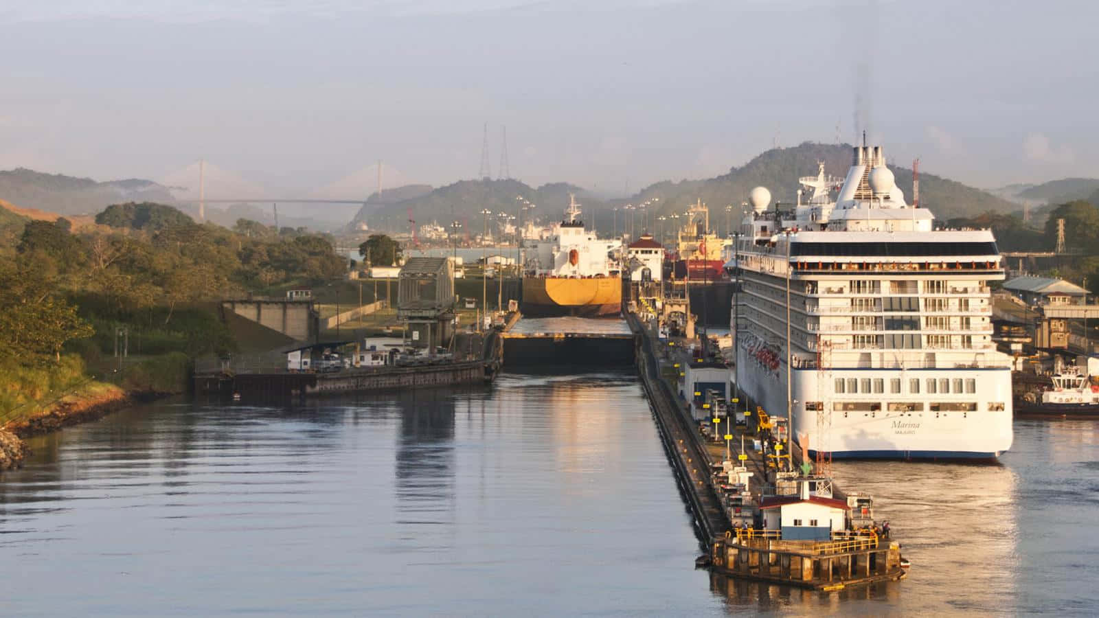 Panama 桌布 壁紙 — 一艘巨大的郵輪在日落時分航行巴拿馬運河，背景是山丘和水閘。